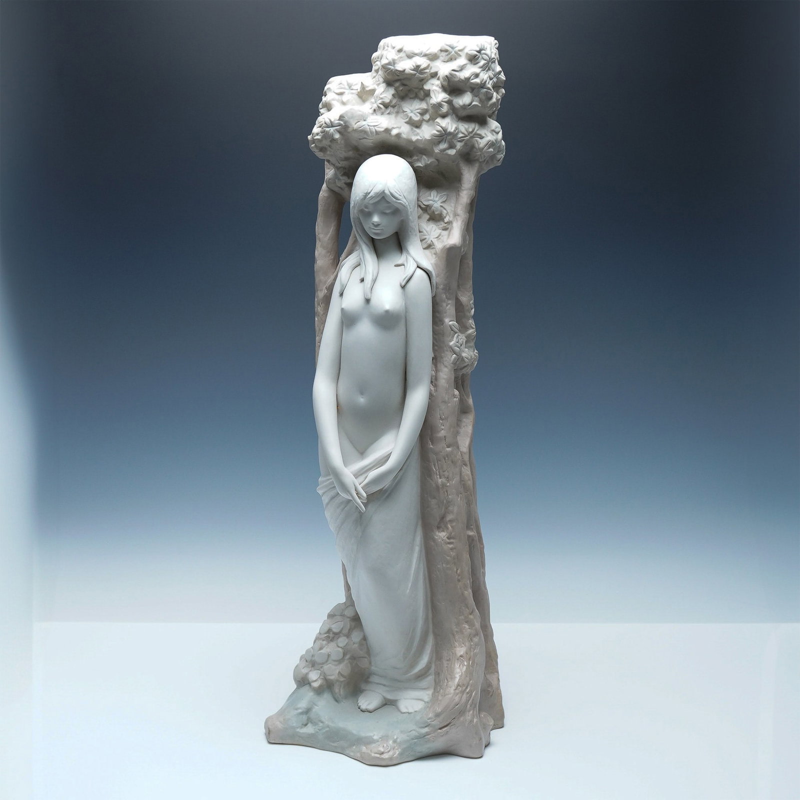Lladro Eve at the Tree Limited Edition Matte Sculpture 01012029: An elegant Lladro Eve at the Tree sculpture, depicting a serene and graceful Eve standing beside a textured tree adorned with delicate blossoms. This limited-edition piece is rendered in Lladro's sign