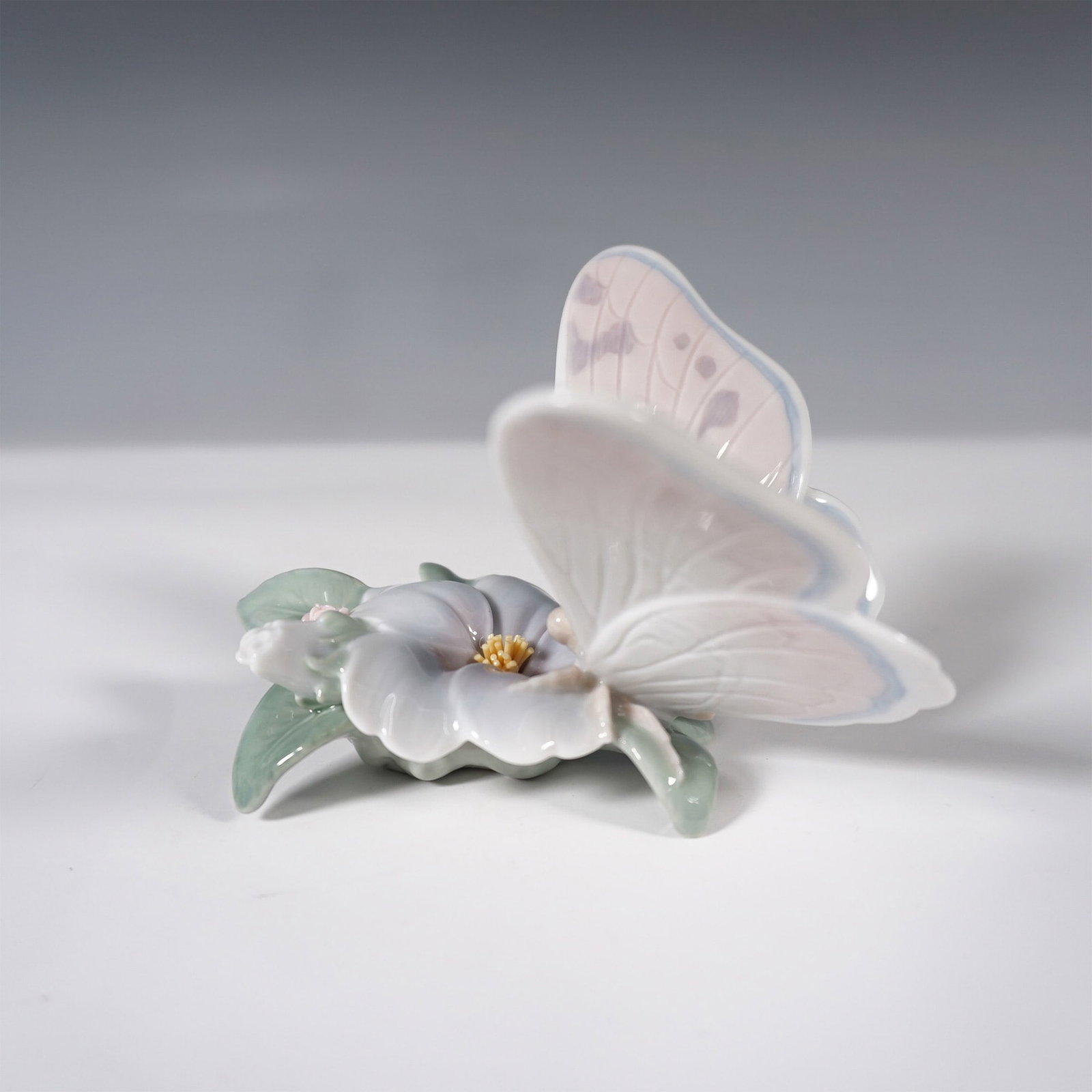 Lladro Porcelain Figurine, Refreshing Pause 1006330: A finely crafted Lladro porcelain figurine featuring a delicate butterfly resting on a flower. This piece showcases soft pastel hues with intricate hand-painted detailing, capturing the grace of natur