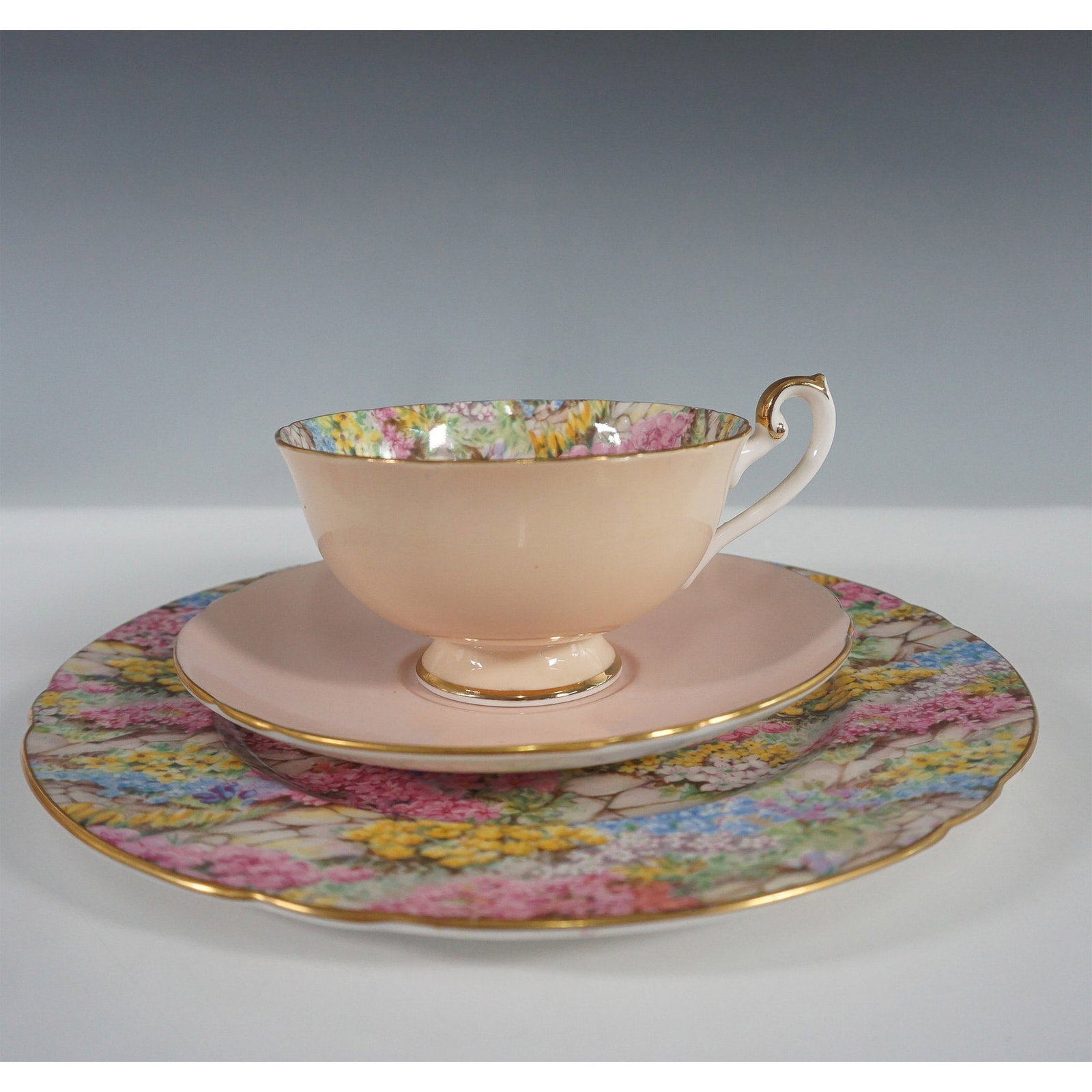3pc Shelley England Rock Garden Trio ? Cup, Saucer, and Plate: Shelley England Rock Garden trio set, featuring a teacup, saucer, and plate in a delicate pastel pink design. The plate and cup interior showcase a vibrant floral chintz pattern depicting a lush rock 