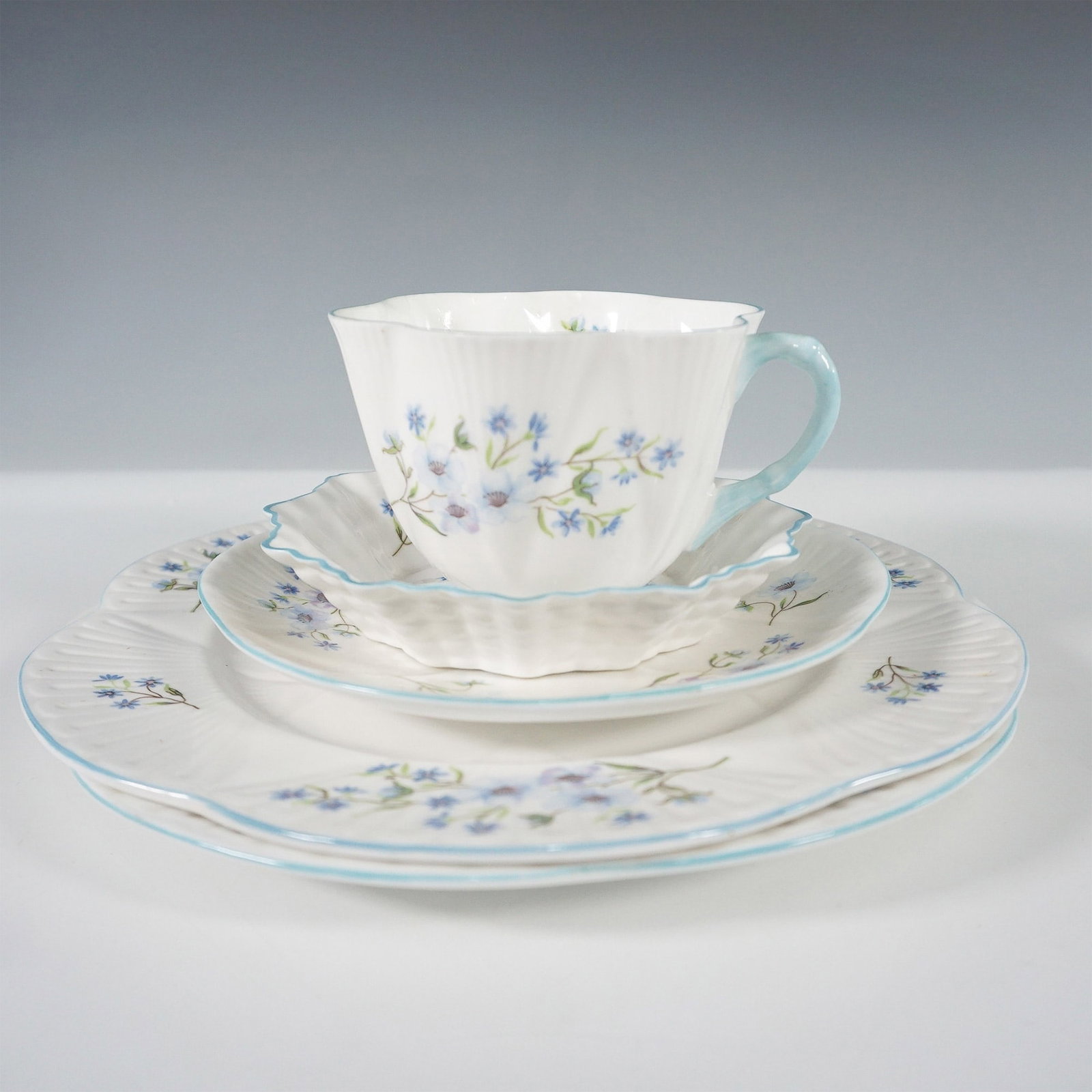5pc Shelley Bone China Tea Set, Blue Rock: A five-piece Shelley bone china tea set in the "Blue Rock" pattern, featuring delicate blue flowers with green foliage. This set includes a teacup, saucer, custard plate, and two dessert plates, all a