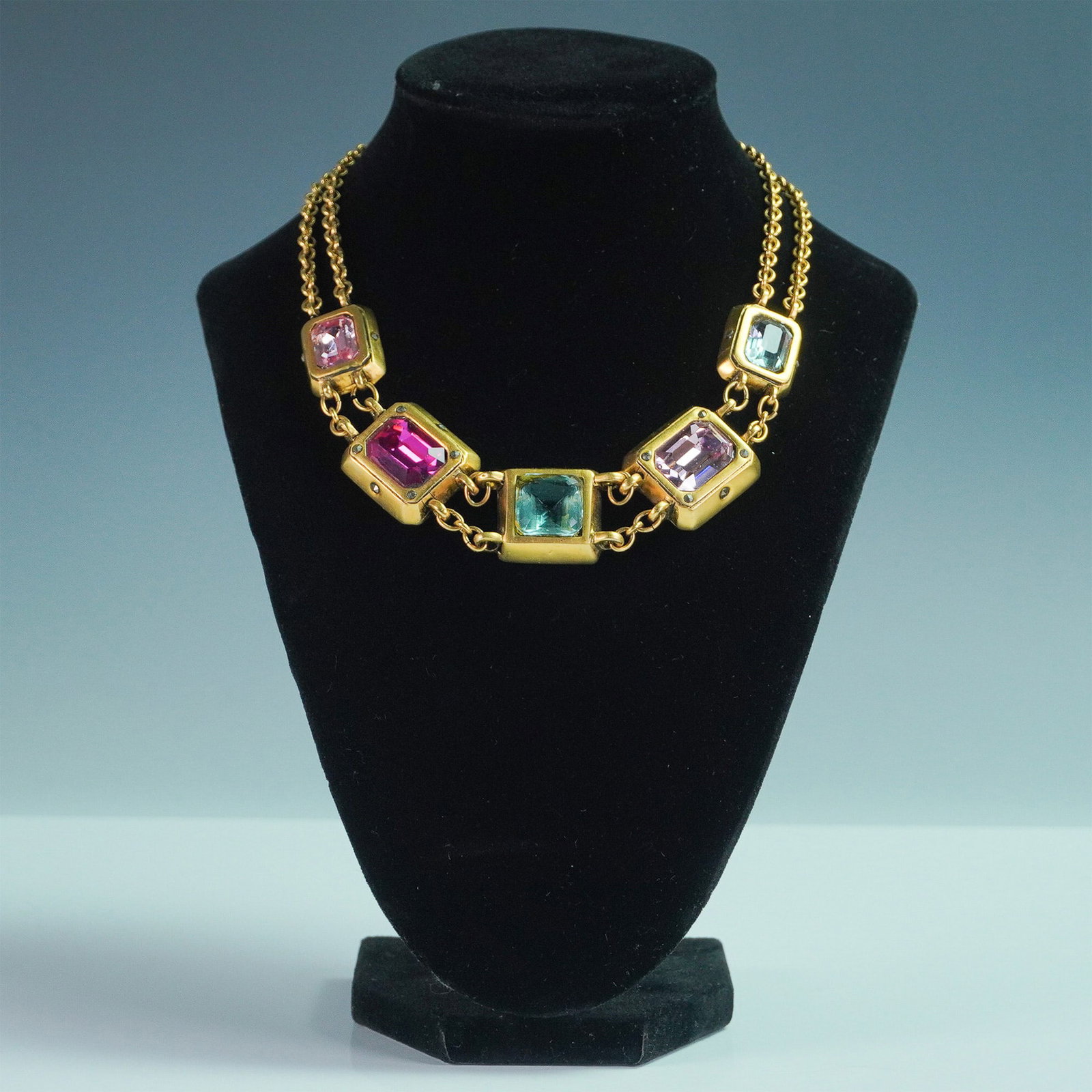 Connie Bates Gold-Tone Necklace with Faceted Jewel-Toned Glass Stones: A striking gold-tone statement necklace featuring square-cut, faceted glass stones in vibrant jewel tones of pink, blue, and green. Each stone is set in a bold metal frame, connected by double-link go