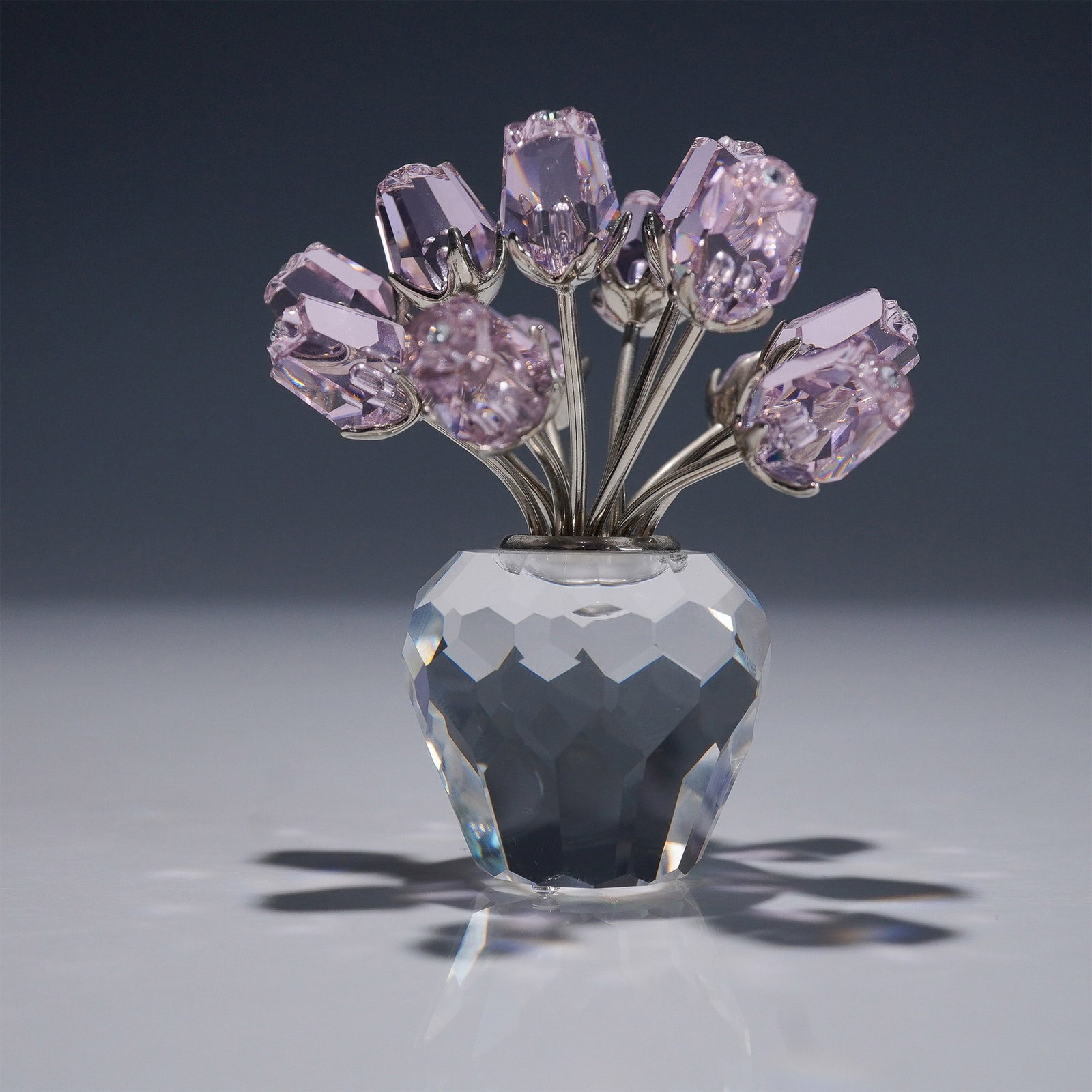Swarovski Crystal Figurine, A Dozen Pink Roses: This retired Swarovski crystal figurine, was part of the In the Secret Garden collection. The elegant piece features a faceted clear crystal vase, rhodium-plated metal stems, and delicate light pink c