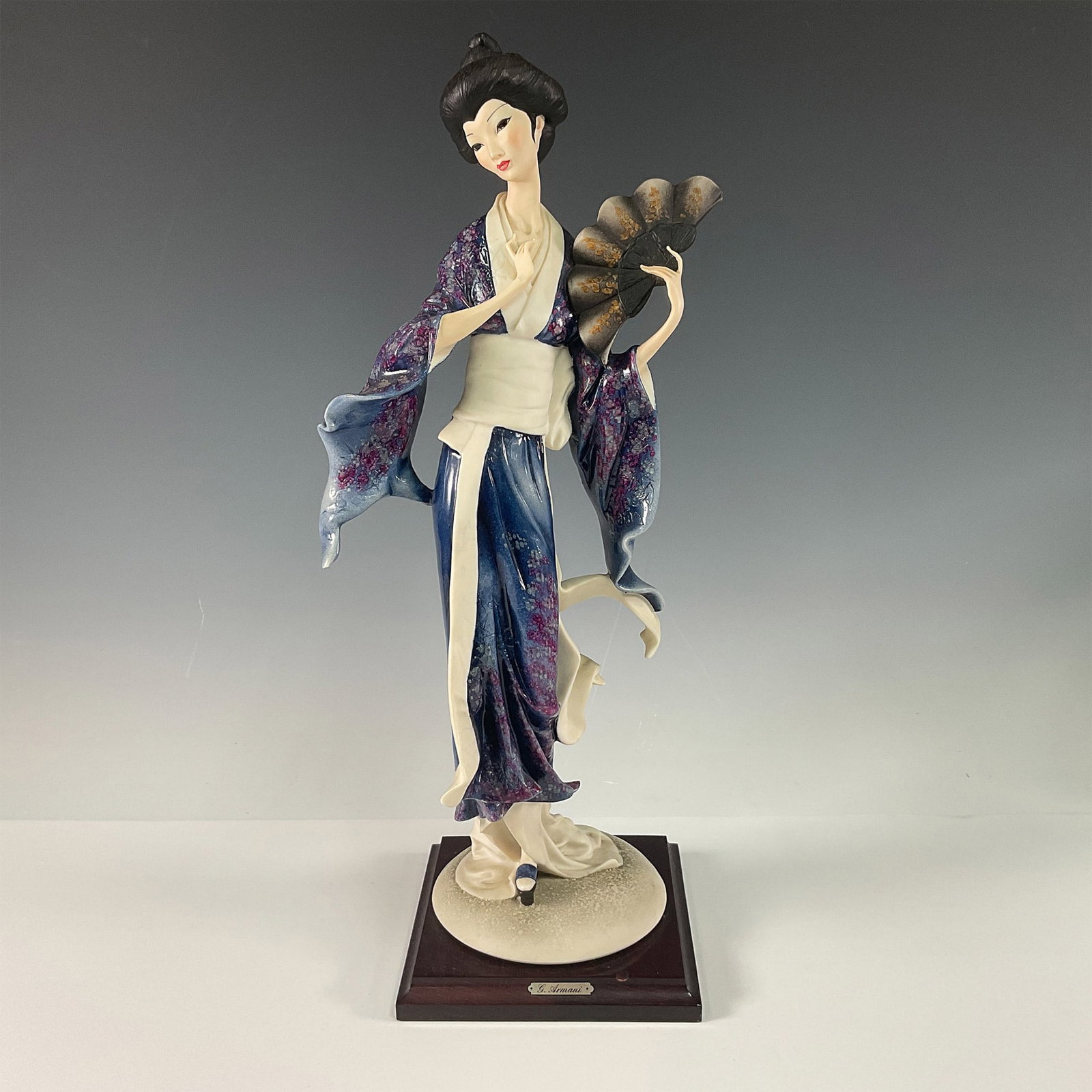 Florence Giuseppe Armani Geisha with Fan Sculpture: This stunning Giuseppe Armani sculpture portrays a graceful geisha holding a fan, embodying elegance and cultural charm. Dressed in a flowing kimono adorned with intricate floral patterns in shades of