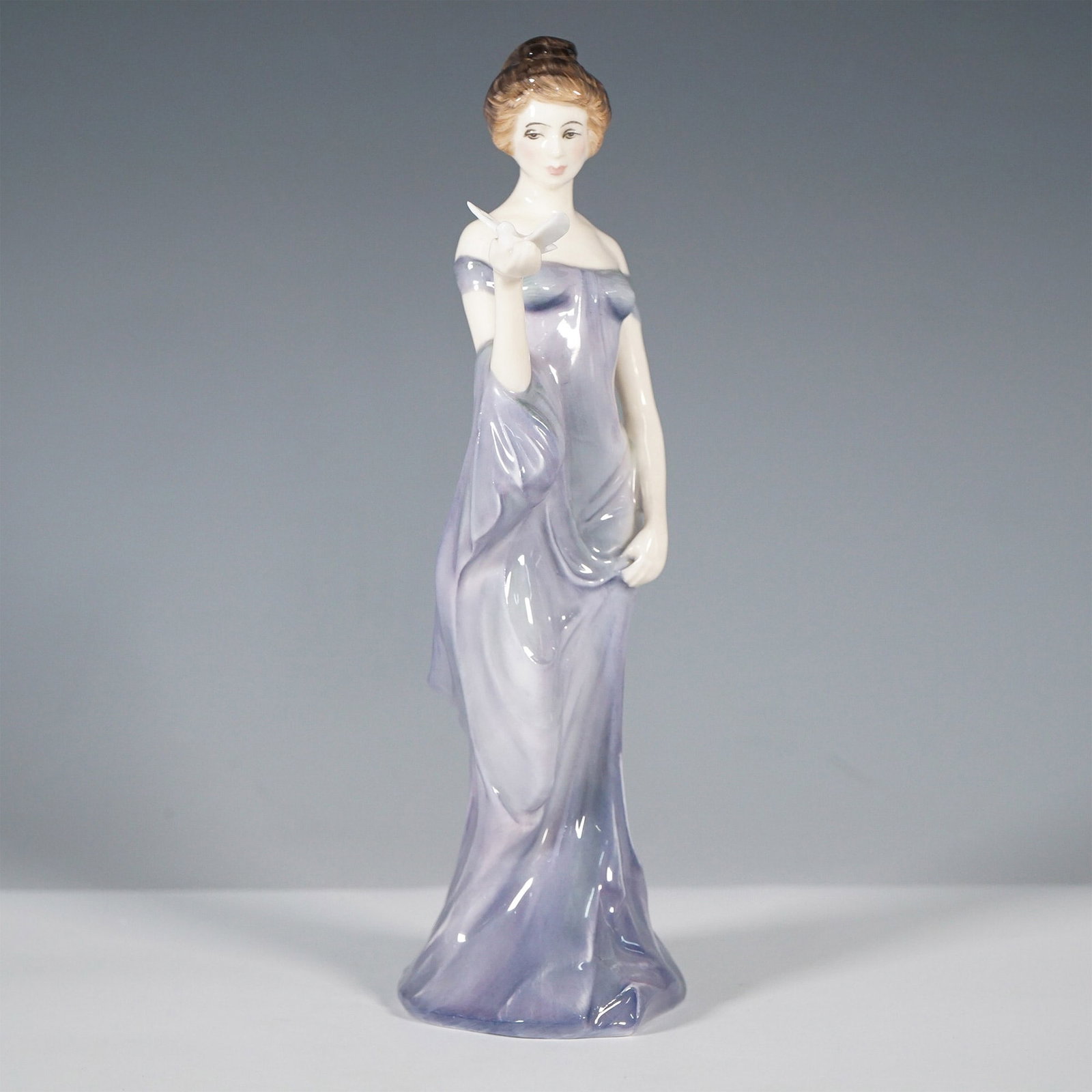 Royal Doulton Bone China Figurine Harmony HN2824: Part of the Classic Pretty Ladies series, this elegant 8-inch figurine features a poised woman in a flowing grey-toned gown with an off-the-shoulder design, delicately holding a white dove. Crafted in