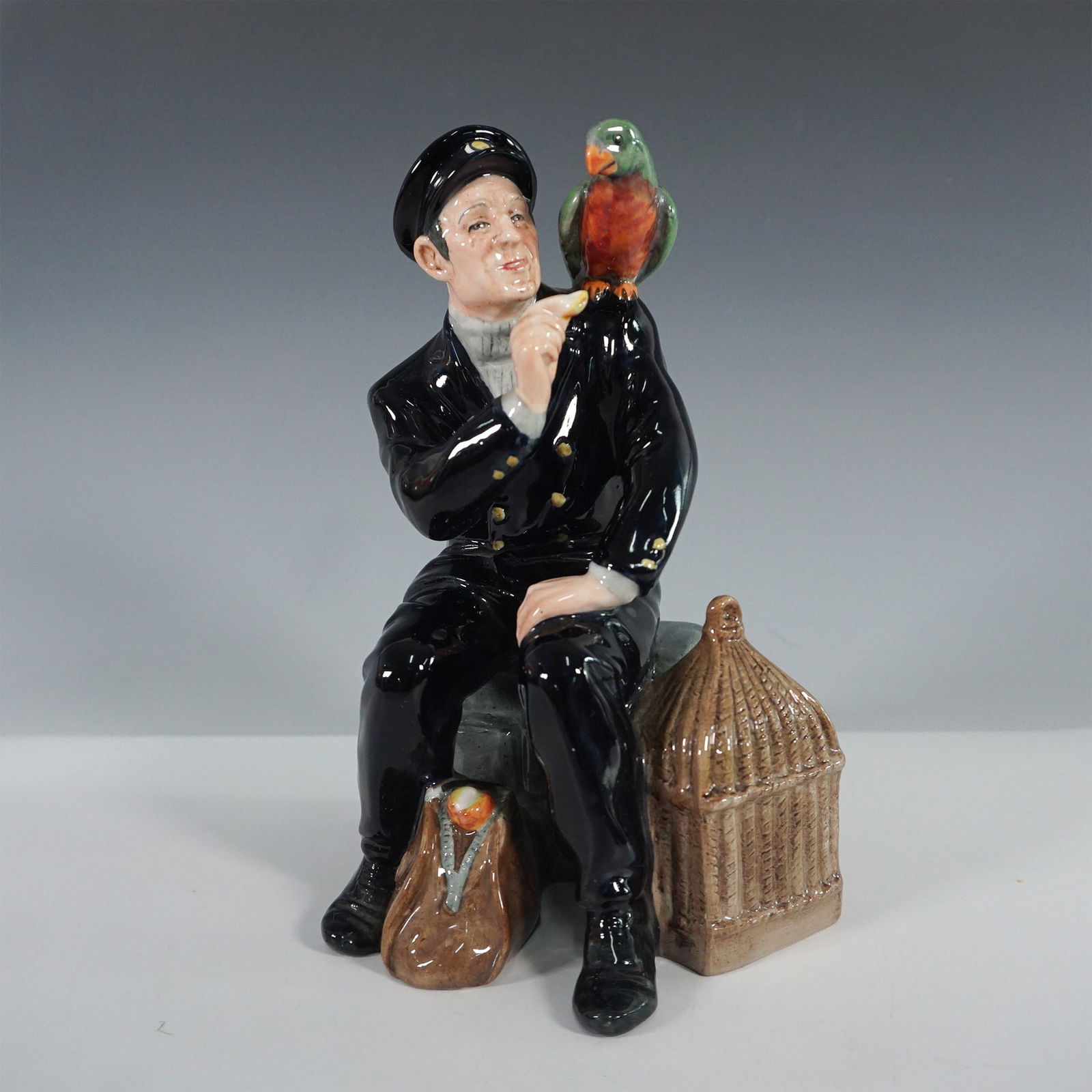 Royal Doulton Figurine, Shore Leave HN2254: Charming Royal Doulton figurine titled Shore Leave (HN2254), designed by Mary Nicholl and issued in 1964. This hand-painted fine bone china sculpture depicts a joyful sailor seated on a stone ledge, e