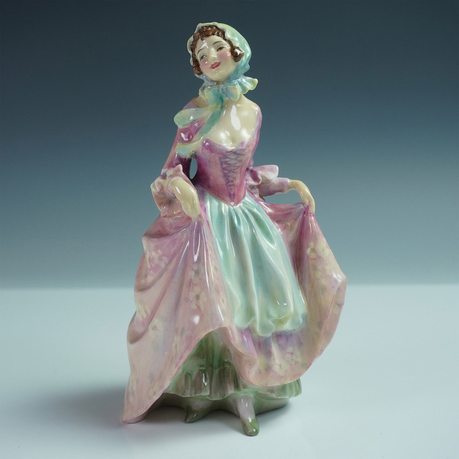 Royal Doulton Bone China Figurine Suzette HN1487: Part of the Harradine Classics series. Featuring a graceful woman in a flowing flowered pink and green dress, she is depicted lifting her gown slightly as she steps forward, exuding charm and movement