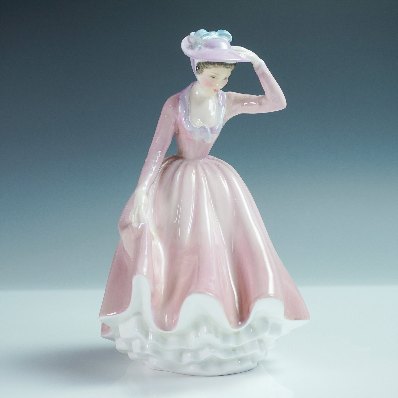Royal Doulton Sweet April Figurine HN2215: A charming Royal Doulton figurine titled Sweet April, model number HN2215. This elegant porcelain piece depicts a young woman in a flowing pink gown with ruffled edges, a wide-brimmed hat adorned with