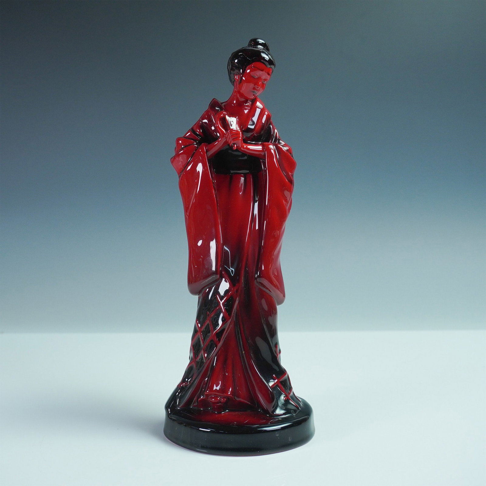 Royal Doulton Flambe The Geisha Figurine HN3229: Royal Doulton The Geisha HN3229 figurine, crafted in a striking deep red flambé glaze, depicts a gracefully posed Japanese woman in a flowing kimono with intricate detailing. Designed by Michael Doul