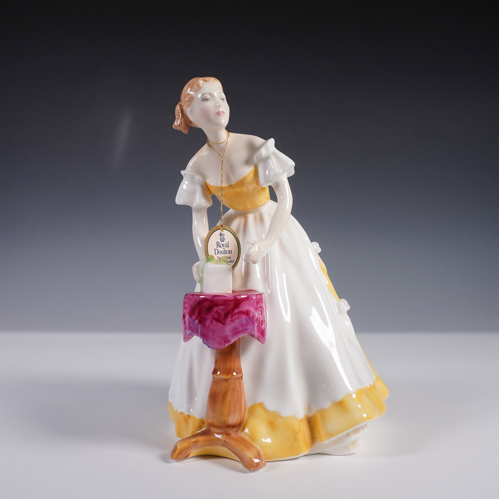 Royal Doulton Figurine, Happy Birthday HN3095: A charming Royal Doulton bone china figurine titled Happy Birthday, model number HN3095. Designed by Pauline Parsons and issued in 1986, this piece features a young woman in an elegant white gown acce