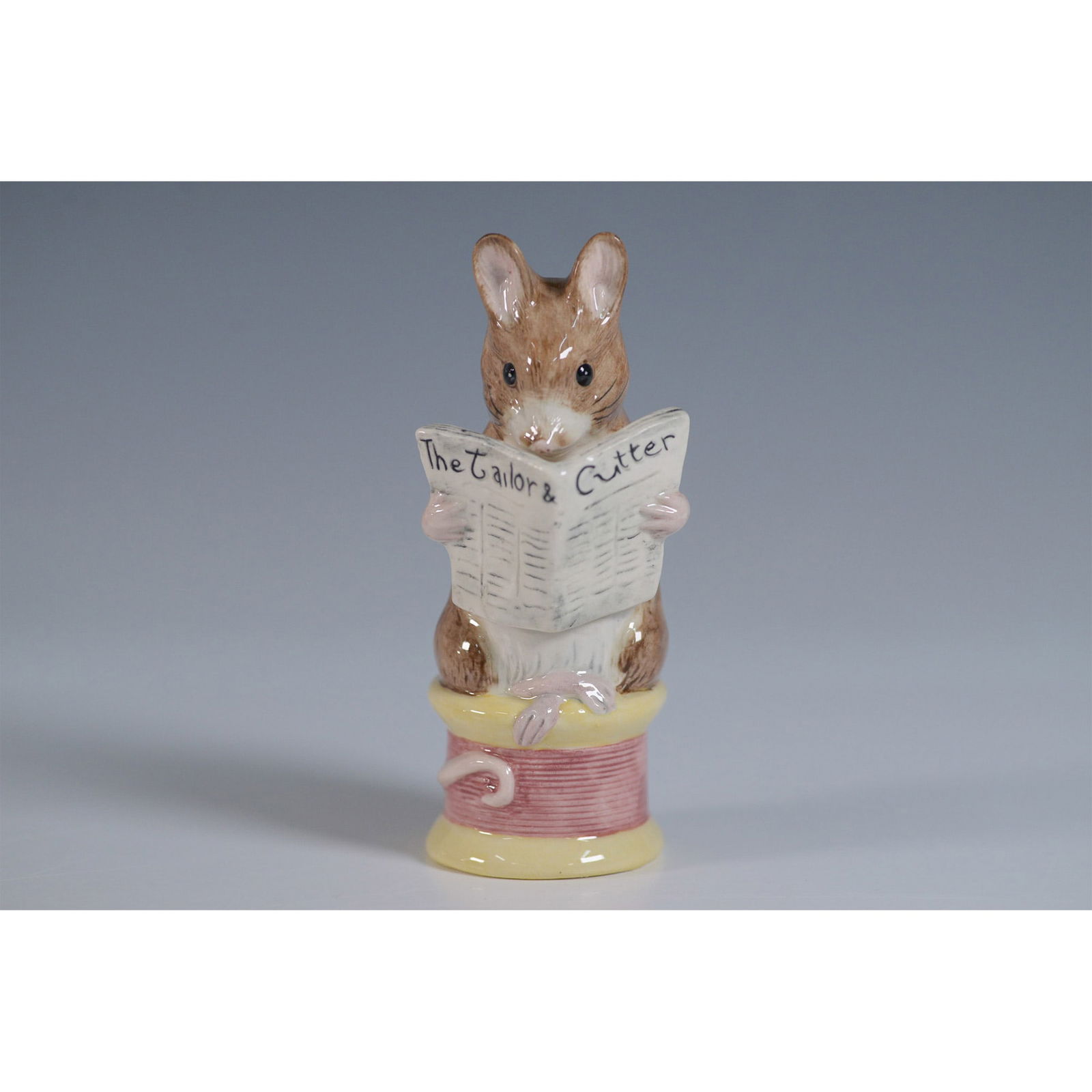 Royal Albert The Tailor of Gloucester Figurine: This charming Royal Albert figurine, titled The Tailor of Gloucester, is part of The World of Beatrix Potter collection. Crafted from fine bone china, it depicts the iconic mouse tailor seated on a sp