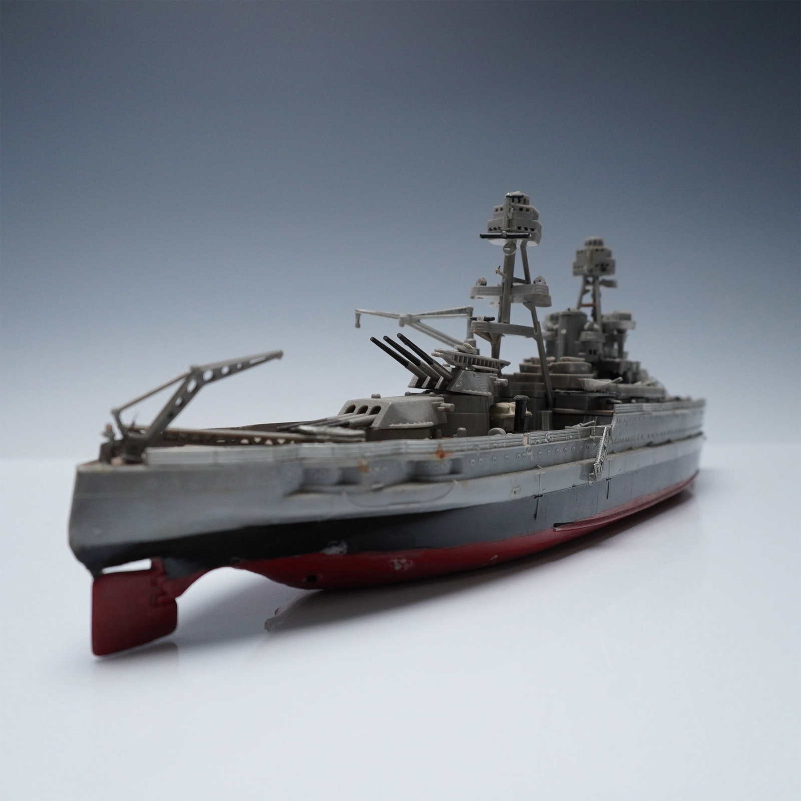 Detailed Scale Model Battleship with Twin Tower Superstructure: This hand-painted model battleship features intricate deck detail and armament, including multiple turrets, cranes, and lifeboats. The dual-tower superstructure suggests an early to mid-20th century n