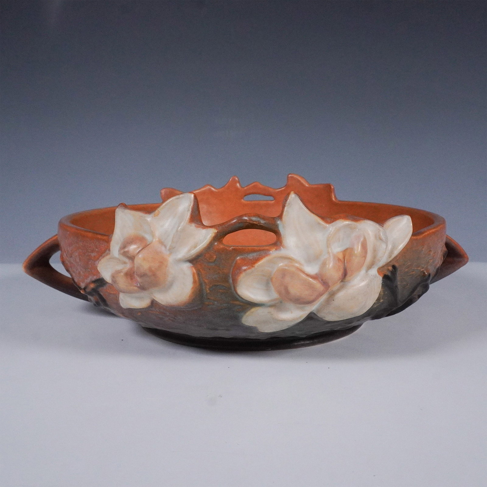 Roseville Pottery Magnolia Bowl, Shape 448-8": Crafted by Roseville Pottery, this Magnolia bowl features the distinctive raised blossom design in warm earth tones with creamy white floral reliefs and green shading at the base. The bowl bears the s