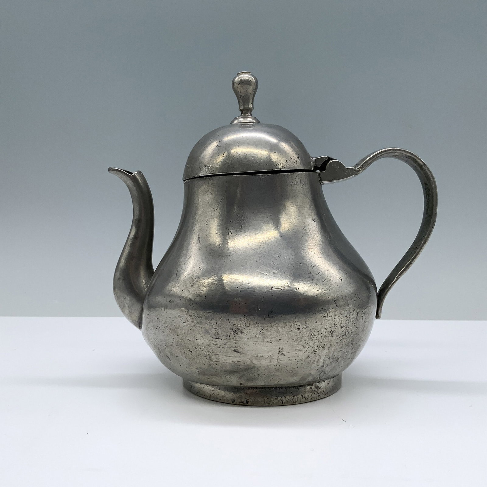 Antique Kamphof Zwolle Pewter Teapot: Classic bulbous body design tea pot, with a curved spout, and an arched handle. The hinged lid is topped with finial in a rounded shape. The teapot sits on a slightly raised circular base. Kamphof Zwo