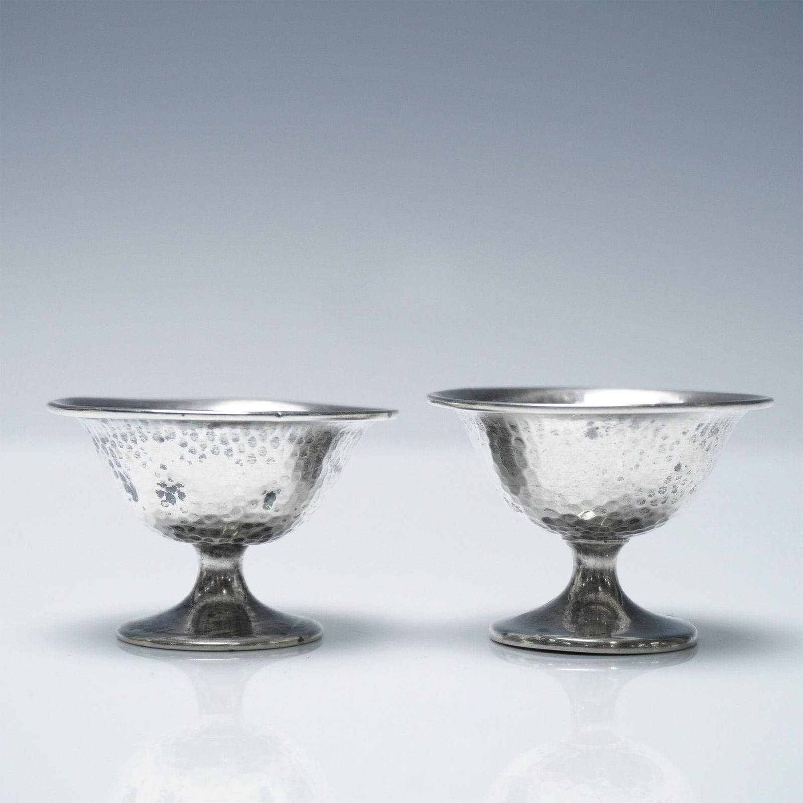 2pc Sterling Silver Egg Cups: A pair of sterling silver egg cups with a hammered texture, marked "STERLING G H F" on the base. Each egg cup measures 1.25"H x 2" in diameter, with a total weight of 14g. Issued: 20th century Dimensi