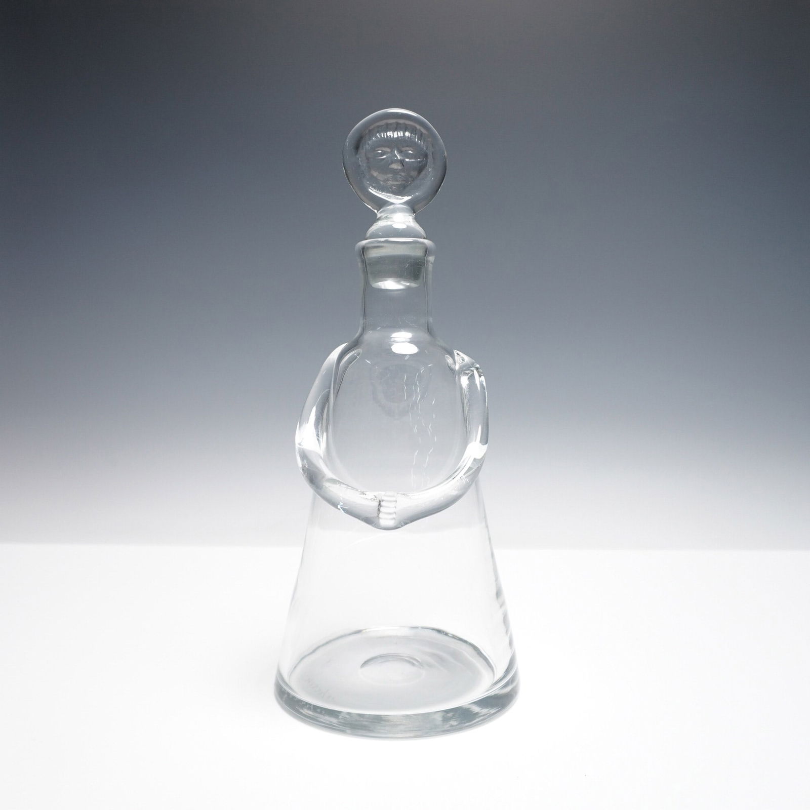 Erik Hoglund for Boda Glass Decanter: Designed by esteemed Swedish glass artist Erik Hoglund for Boda, this remarkable glass decanter showcases his signature sculptural aesthetic. The conical form is adorned with an applied glass arm deta