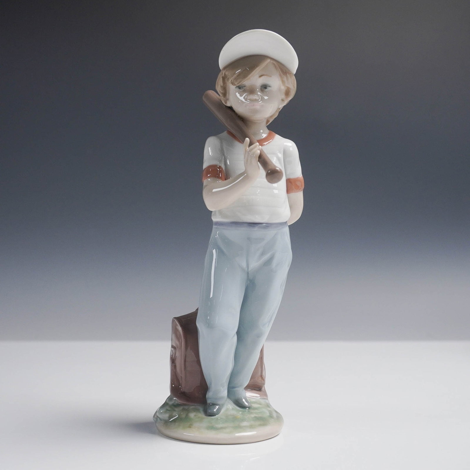Can I Play? 1007610 - Lladro Porcelain Figurine: This Lladro Collectors Society figurine, Can I Play?, features a young boy in a baseball cap leaning on a bat, poised with a hopeful expression. The sculpted figure conveys a sense of anticipation and