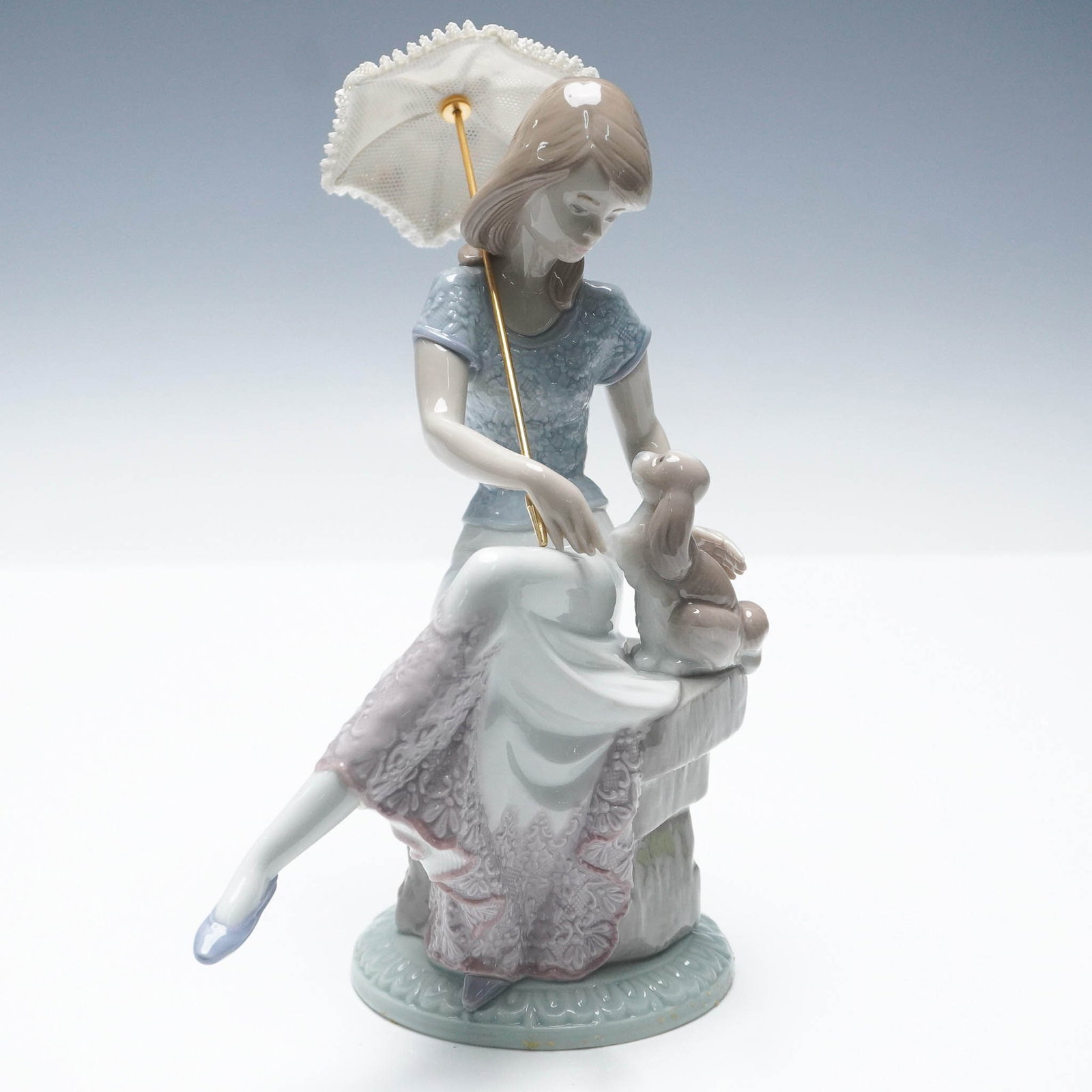 Picture Perfect 1007612 - Lladro Porcelain Figurine: Issued and retired in 1991, this Lladro porcelain figurine titled Picture Perfect (7612) depicts a young woman seated on a stone bench with a parasol in one hand and a puppy in the other. She wears a 