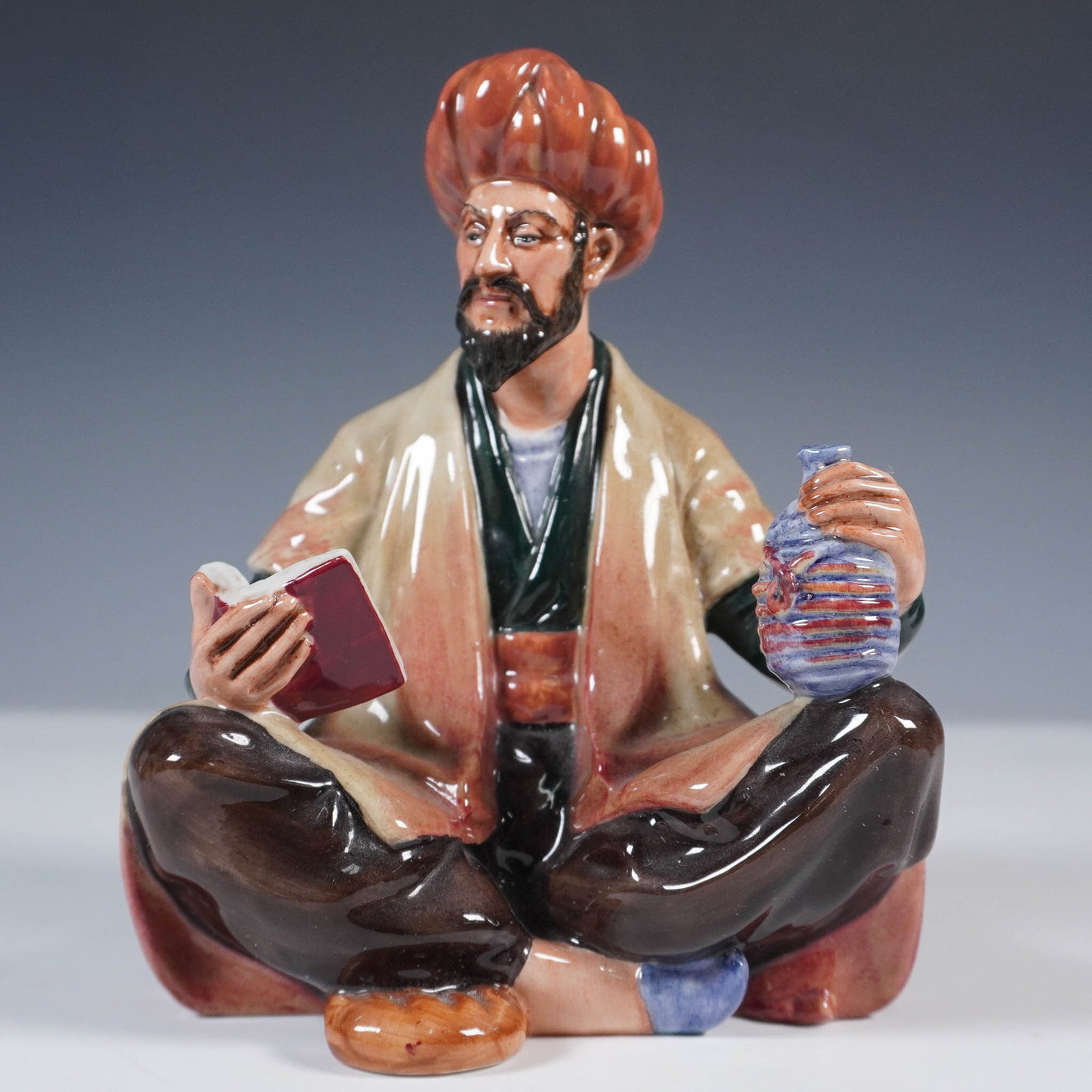 Royal Doulton Figurine, Omar Khayyam HN2247: This hand-painted figure depicts the famed Persian poet seated cross-legged, holding a book in one hand and a jug in the other. Finished in a high-gloss glaze, the figurine showcases Khayyam in tradit