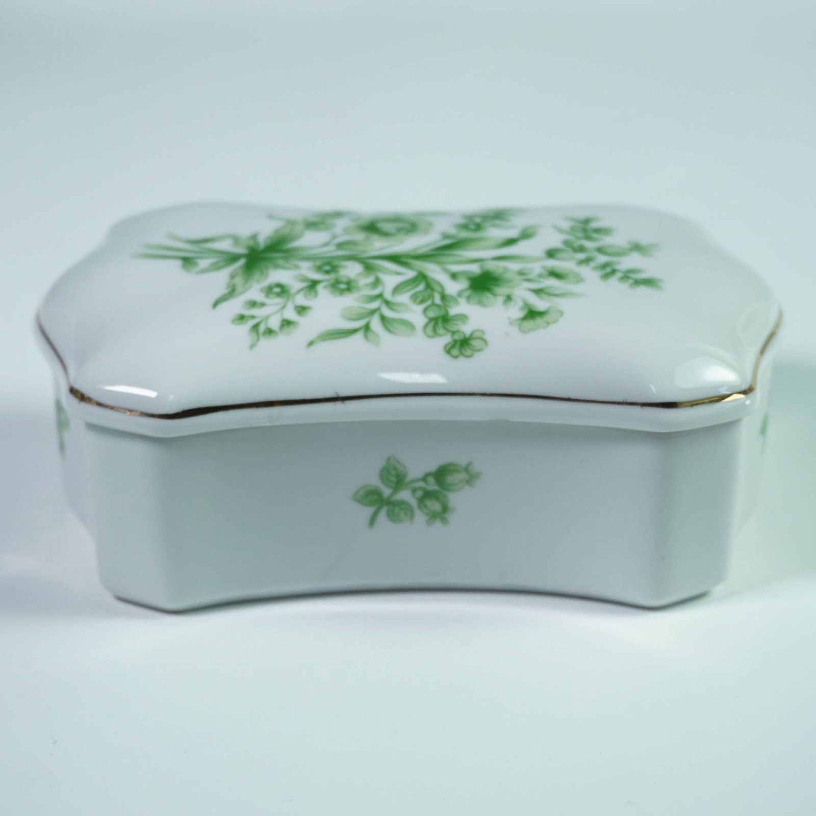 Hollohaza Hungary Porcelain Lidded Box with Green Floral Design: Porcelain lidded trinket or vanity box by Hollohaza, Hungary, featuring a soft rectangular form with gently scalloped edges and a domed lid. Decorated in a delicate green floral motif with fine gold t