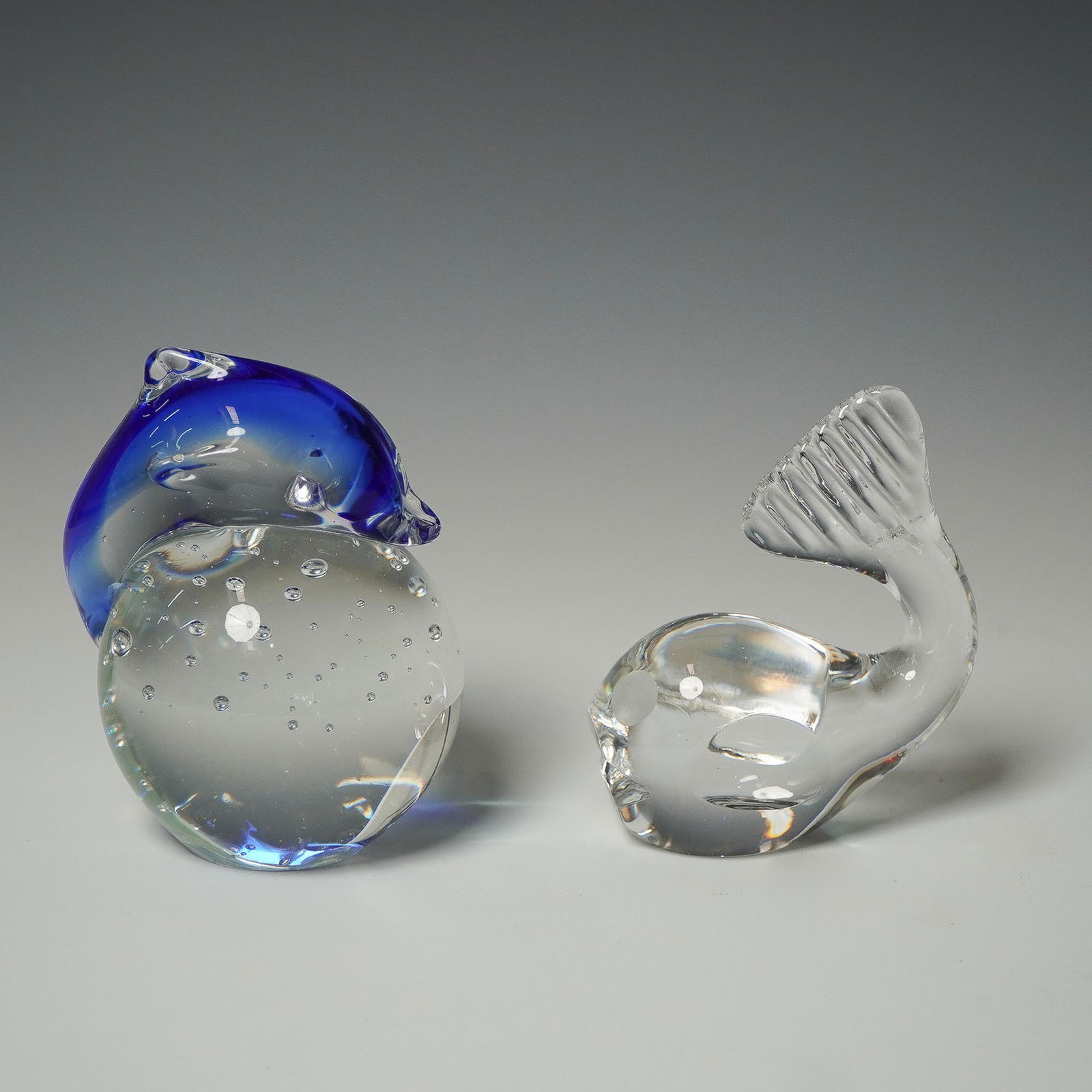 2pc Art Glass Figurines, Spode Whale & Dolphin Paperweight: Pair of art glass figurines including a clear Spode whale sculpture, measuring approximately 3.75"L, and a blue and clear dolphin balanced on a clear bubble-infused sphere, measuring approximately 4"H