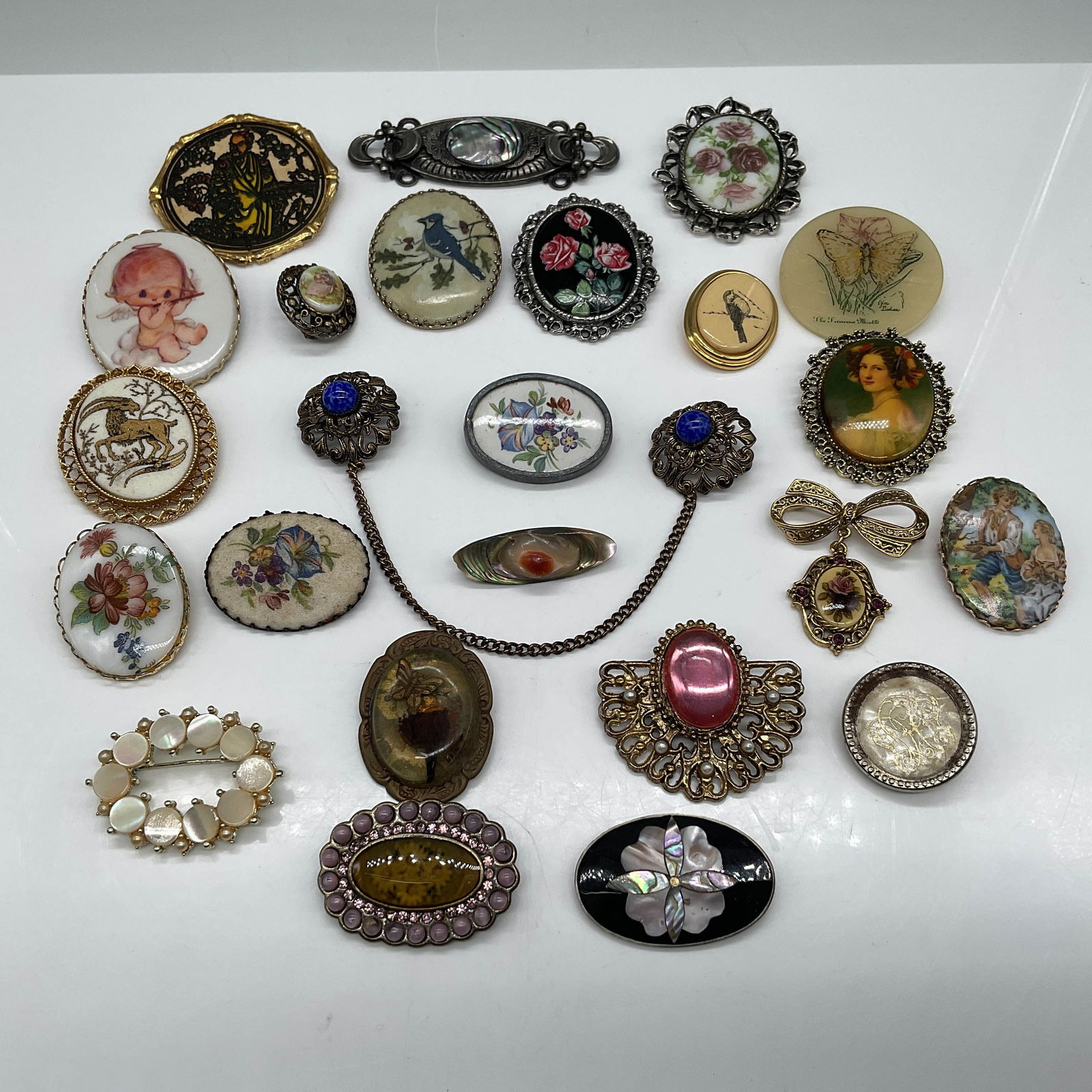 24pc Vintage Costume Jewelry Brooch Collection: A curated collection of vintage costume jewelry brooches, featuring 24 pieces of diverse styles and materials. This lot includes a mix of hand-painted porcelain, mother-of-pearl, metalwork, and cameo