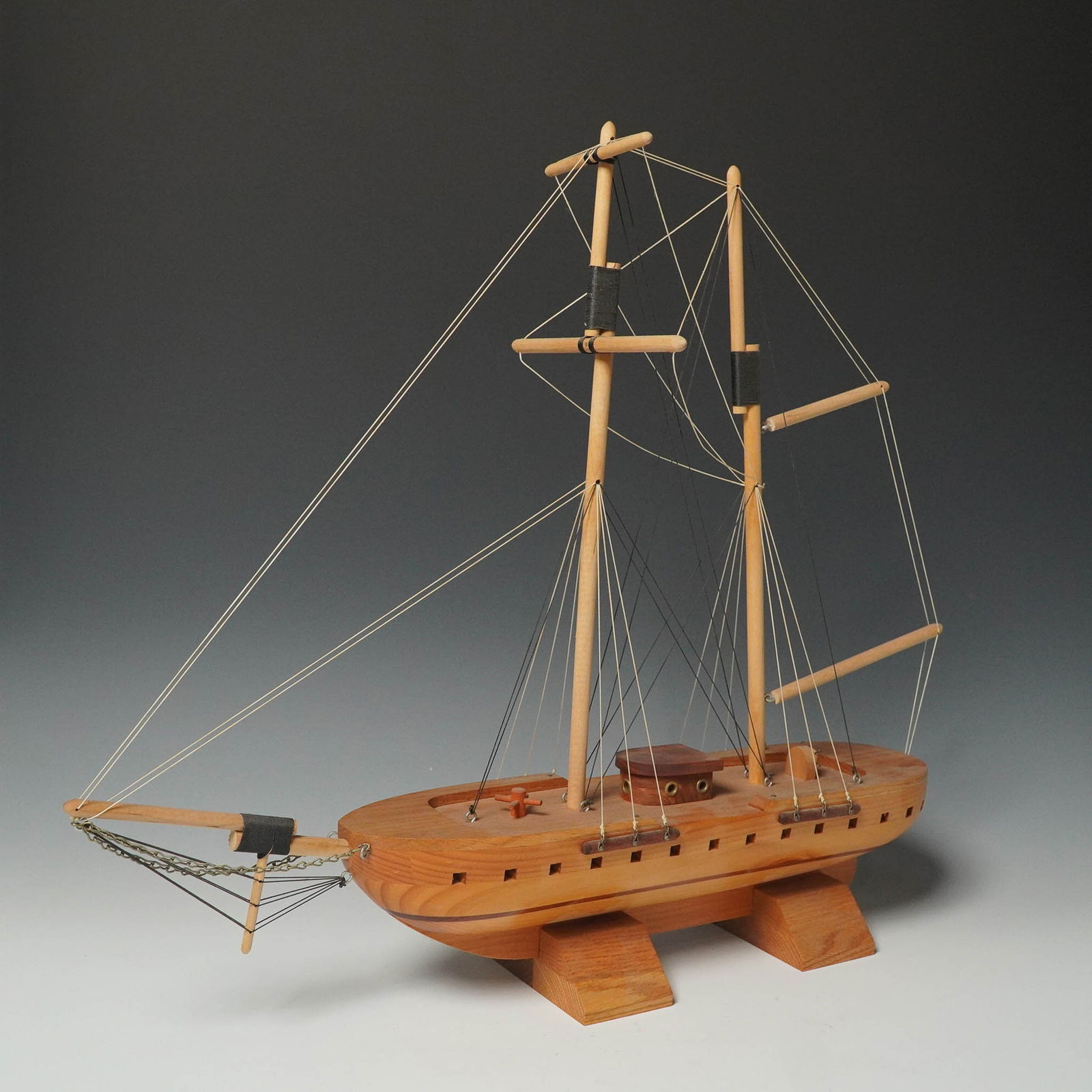 Wood Model Sailing Ship, Two-Mast Display with Base: Handcrafted wooden model ship featuring a two-mast rig with intricate string rigging, chain accents, and a hull with carved port details. The deck includes a raised cabin with faux portholes and a sma
