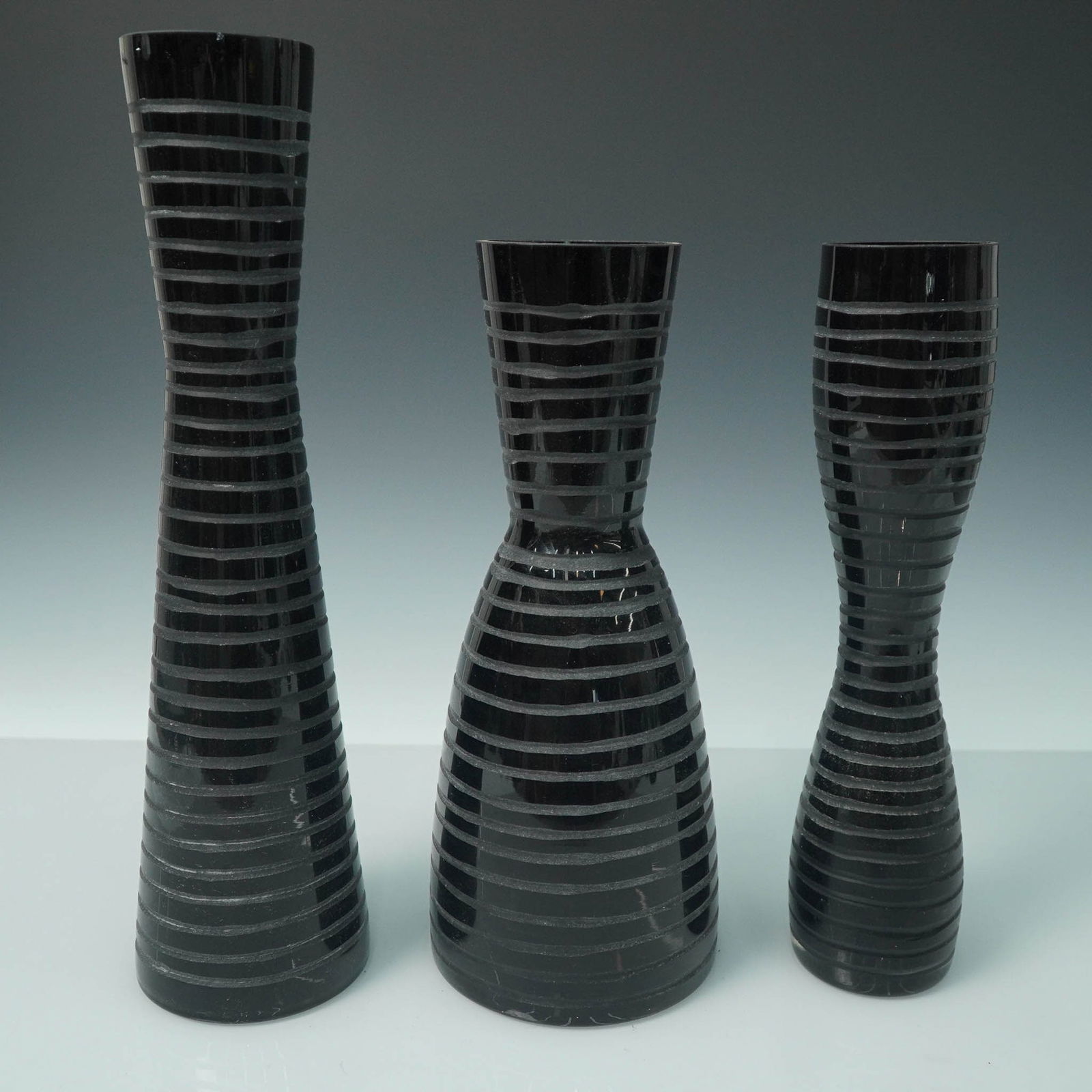 3pc Black Glass Vases with Striped Banding: Group of three black glass vases featuring horizontal textured banding and subtly varied silhouettes. Each vase has a glossy finish with frosted stripe accents, lending a contemporary touch to the mid