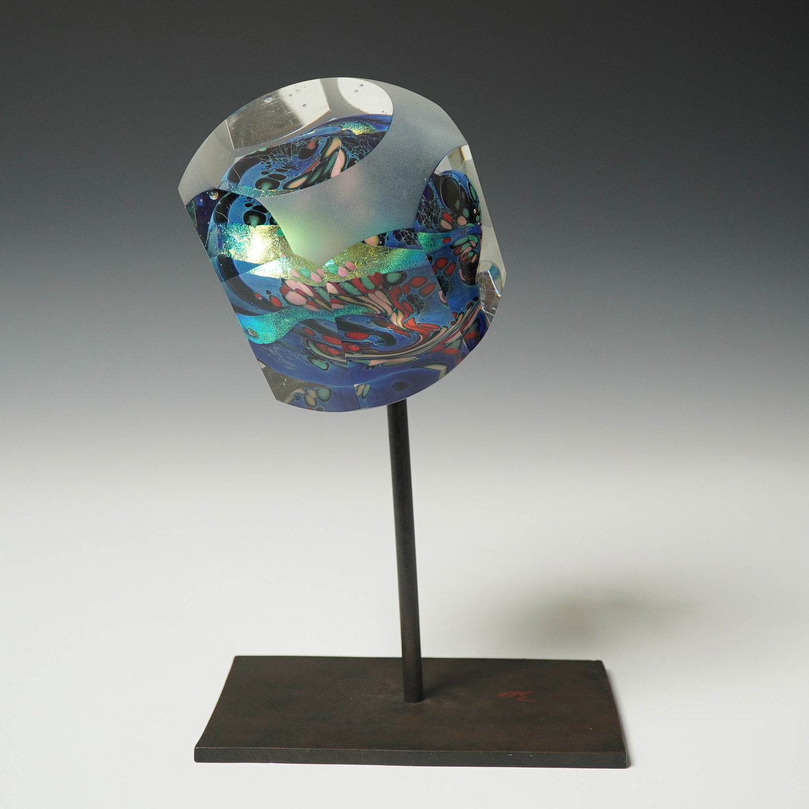 Art Glass Sculpture on Iron Stand, Attributed to Karg Studio: Vibrant contemporary art glass sculpture featuring a faceted cylindrical form with frosted and polished surfaces, showcasing vivid swirls of blue, green, pink, and metallic hues. The internal design r