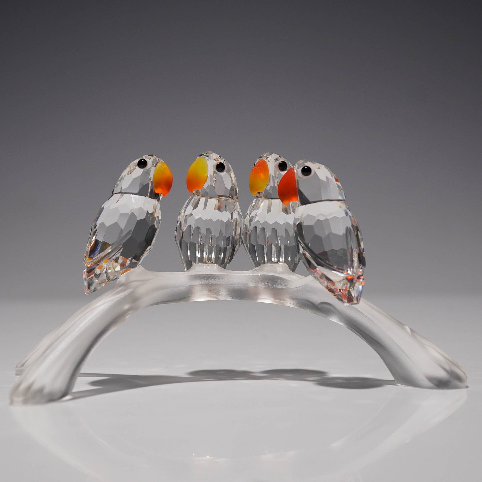 Swarovski Crystal Figurine, Lovebirds Baby 199123: This piece was part of the Feathered Beauties theme group. The design features four faceted clear crystal baby lovebirds perched on a frosted arching branch with three prongs. Each bird is detailed wi
