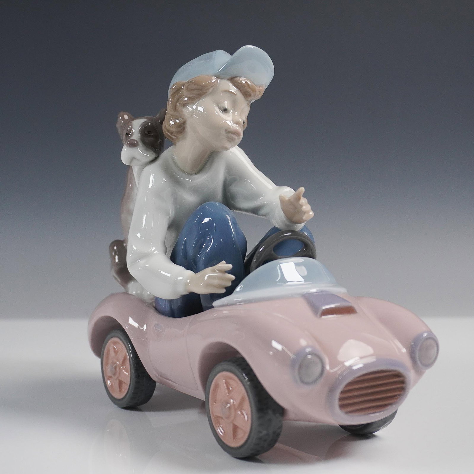 Lladro Porcelain Figurine Out for a Spin 01005770: Lladro figurine titled Out for a Spin, model 01005770, sculpted by Joan Coderch. Issued in 1991 and retired in 1994, this playful piece features a young boy driving a pastel pink toy car with his loya