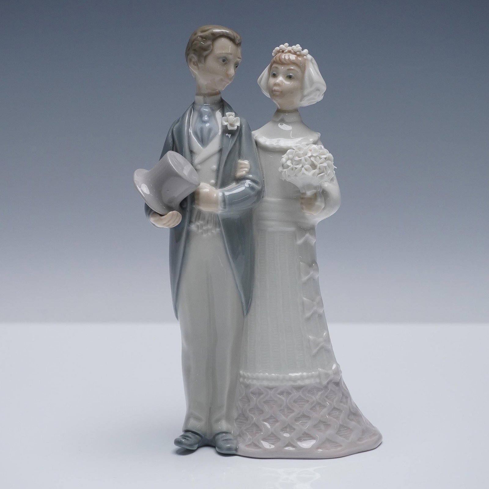 Lladro Porcelain Figurine, Wedding 1004808: This porcelain figurine features a bride and groom standing arm in arm. The groom is shown in formal attire with a tailcoat and top hat in hand, while the bride is adorned in a textured gown and veil,