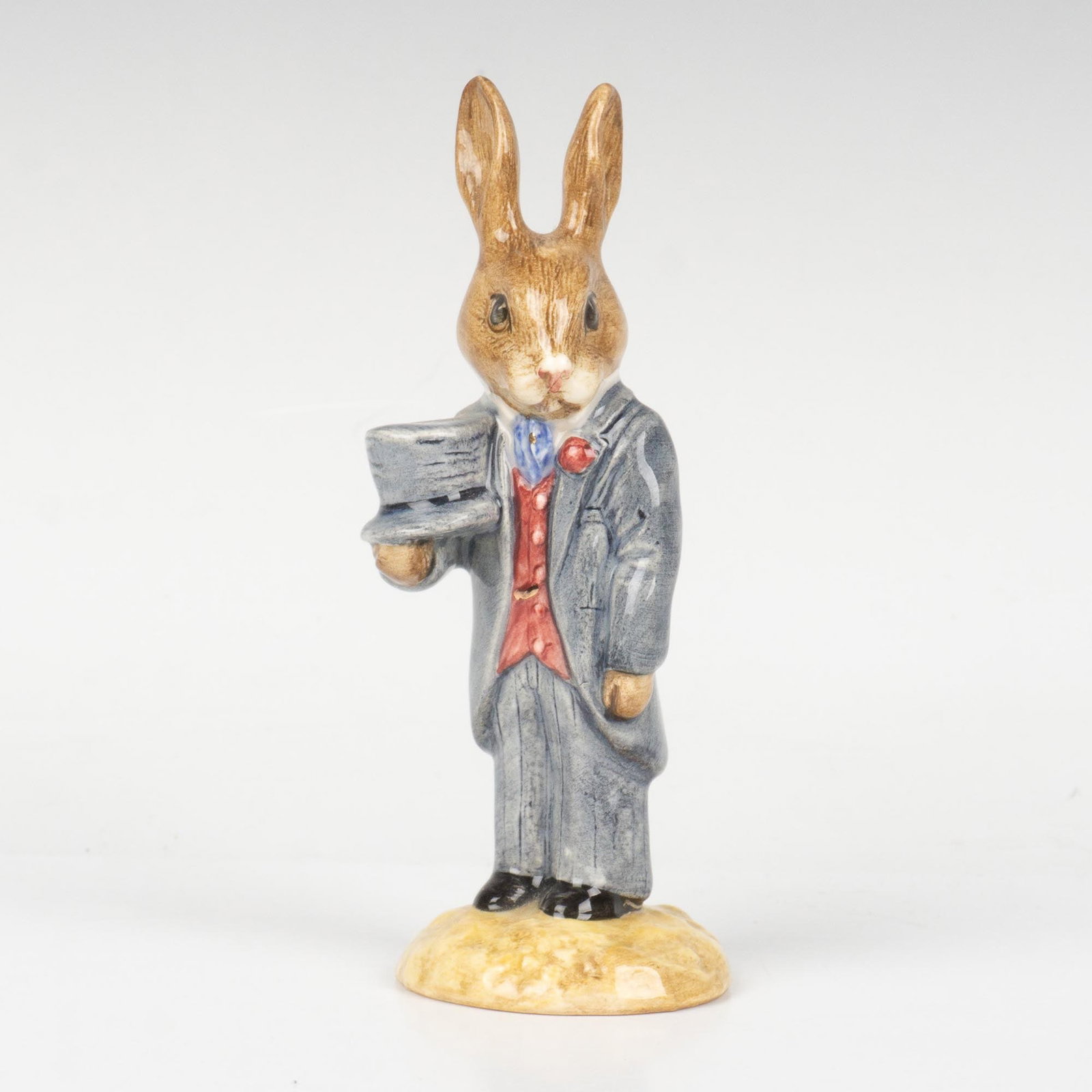 Groom DB102 - Royal Doulton Bunnykins: A male bunny dressed in formal wedding attire and carrying their hat. Grey and red coloration. Royal Doulton backstamp. Artist: G. Tongue Issued: 1991 - 2001 Dimensions: 4.5"H Country of Origin: Engla