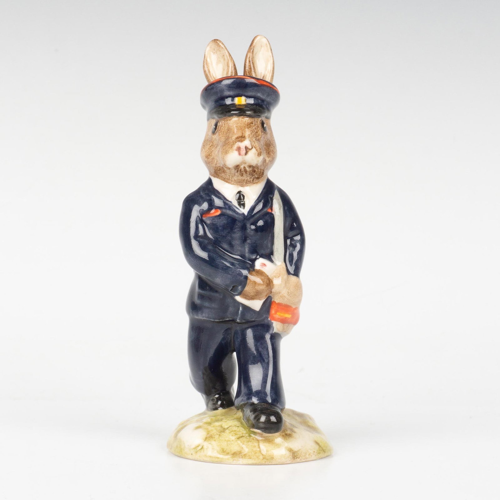 Postman DB76 - Royal Doulton Bunnykins: A mail worker on the way to deliver letters. Dressed in a navy blue uniform and carrying a brown satchel. Royal Doulton backstamp. Artist: G. Tongue Issued: 1989 - 1993 Dimensions: 4.5"H Country of Or