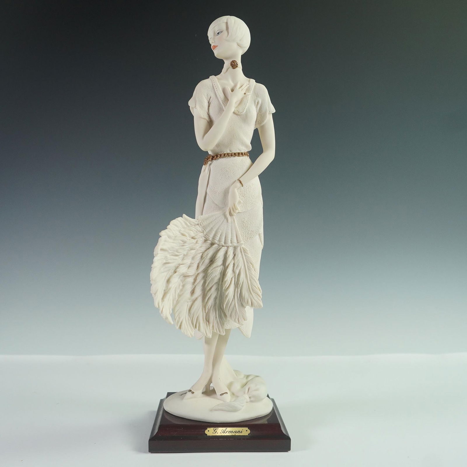 Giuseppe Armani Capodimonte Figurine, Woman with Fan: A Florence Sculture d'Arte figurine by Giuseppe Armani, portraying an Art Deco woman in a textured dress holding a large feathered fan. Finished in matte tones with gold accents, mounted on a wooden b