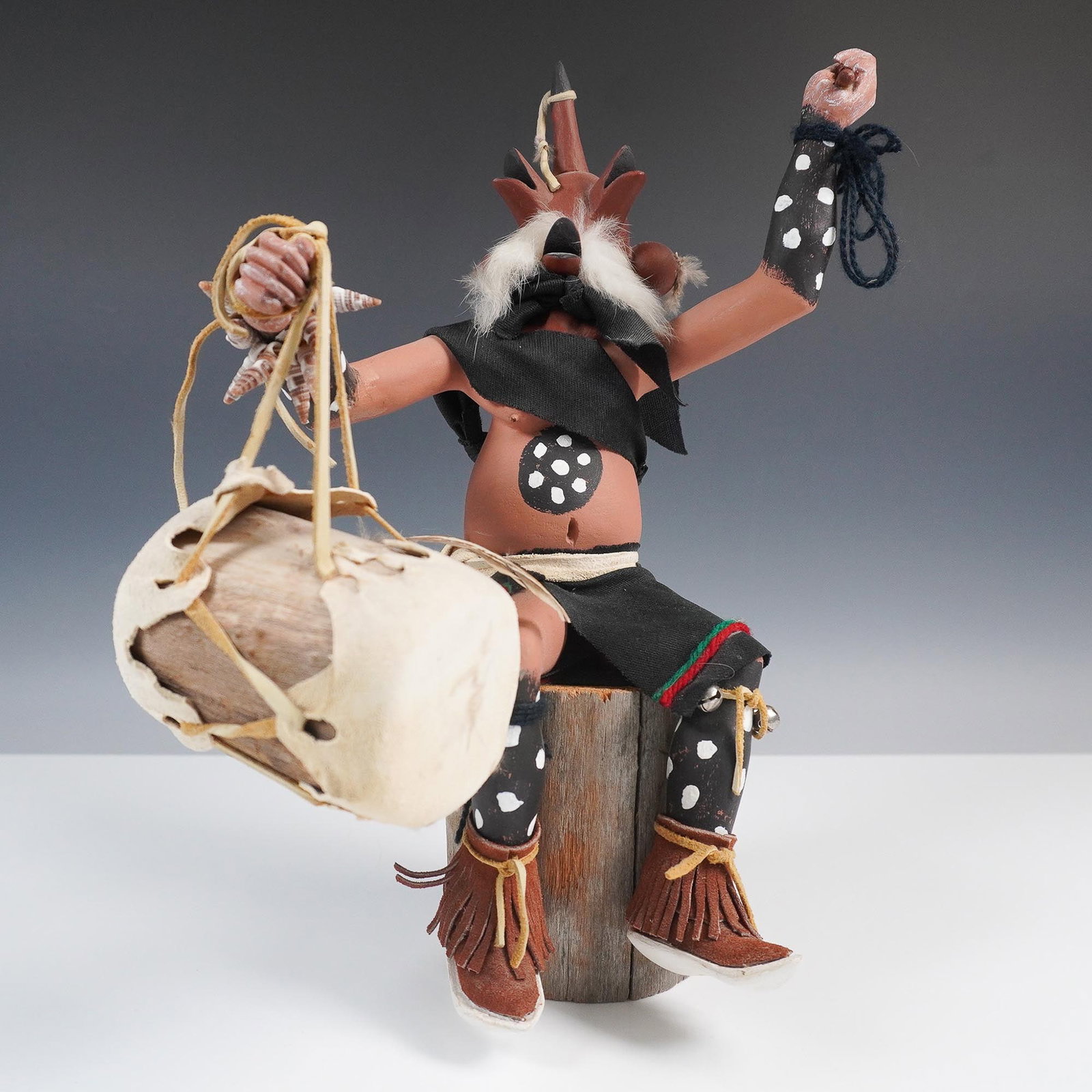 Native American Kachina Drummer Figure by Larry Hobbs, Signed: Handcrafted Native American Kachina figure seated on a natural wood log base, by artist Larry Hobbs. The figure features traditional elements such as feathers, fur accents, painted body details, leath