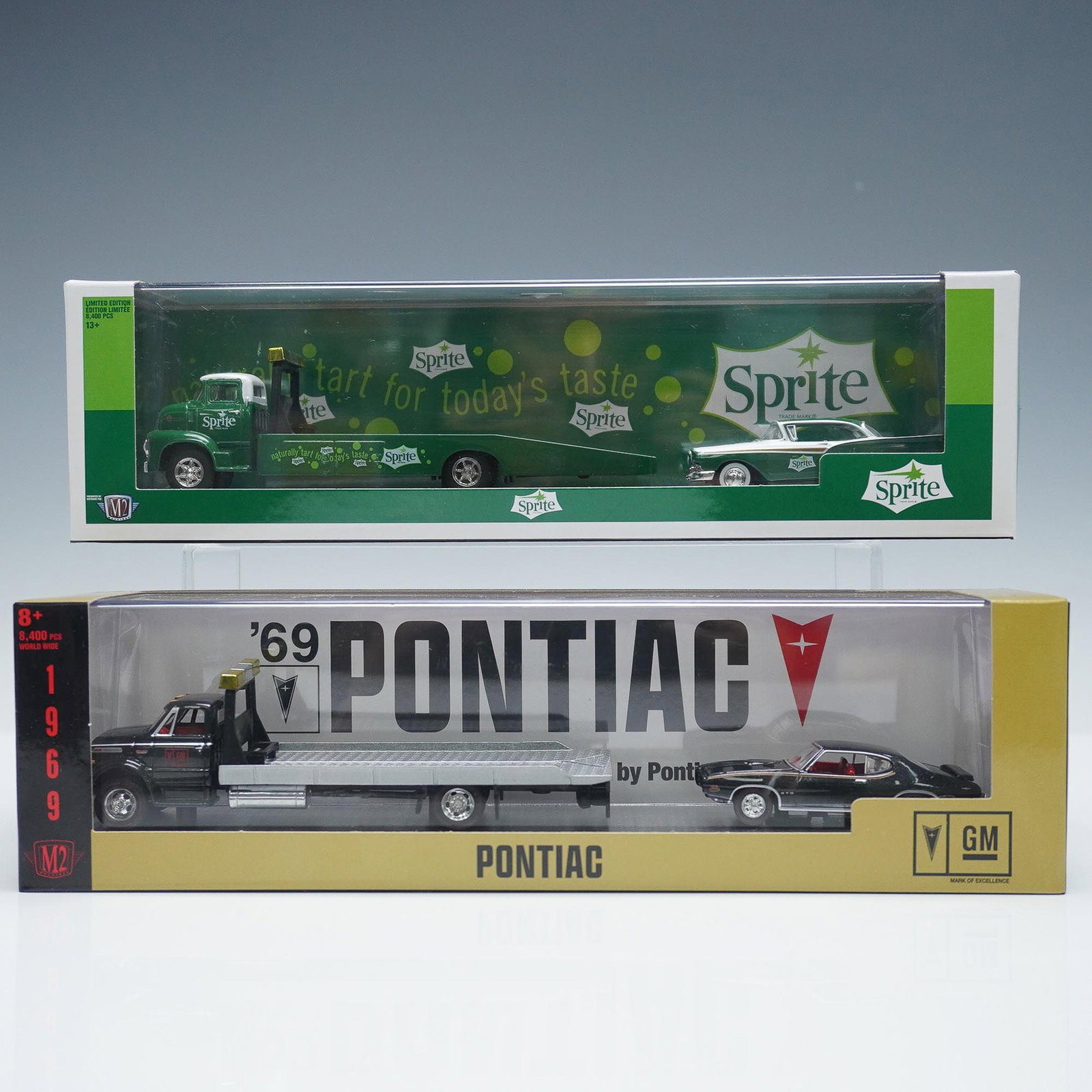2pc M2 Machines Die-Cast Car and Transporter Sets, Sprite and Pontiac: Pair of M2 Machines collectible sets, each featuring a car and transporter truck in sealed display packaging. Includes a Sprite themed set with a vintage green Sprite delivery truck and matching car, 