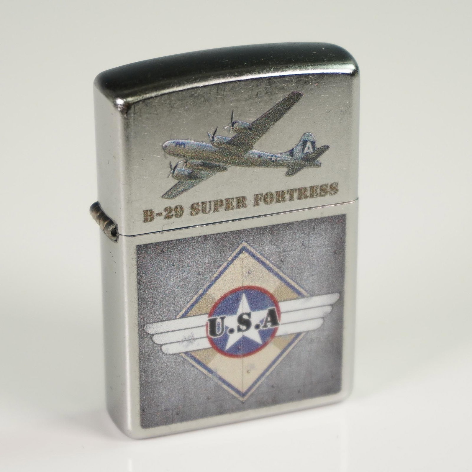 Zippo American Silver-Metal Lighter, B-29 Super Fortress - U.S.A.: The upper section depicts a detailed image of the B-29 Super Fortress in flight, with "B-29 SUPER FORTRESS" printed below. The lower section features a U.S.A. emblem with wings, placed over a metallic