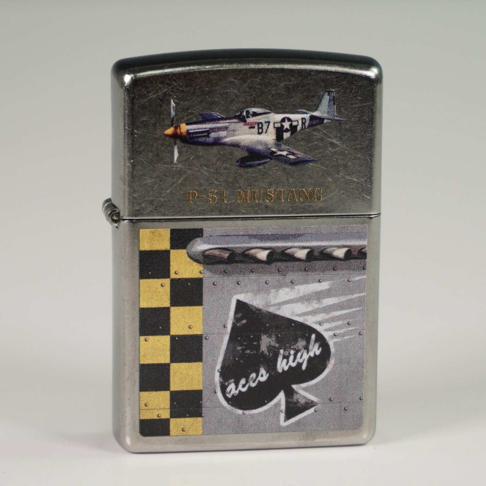 Zippo American Silver-Metal Lighter, P-51 Mustang - Aces High: Zippo American silver-metal lighter featuring artwork inspired by the P-51 Mustang aircraft. The lighter displays a depiction of the P-51 Mustang marked "B7" flying against a metallic backdrop. Below,