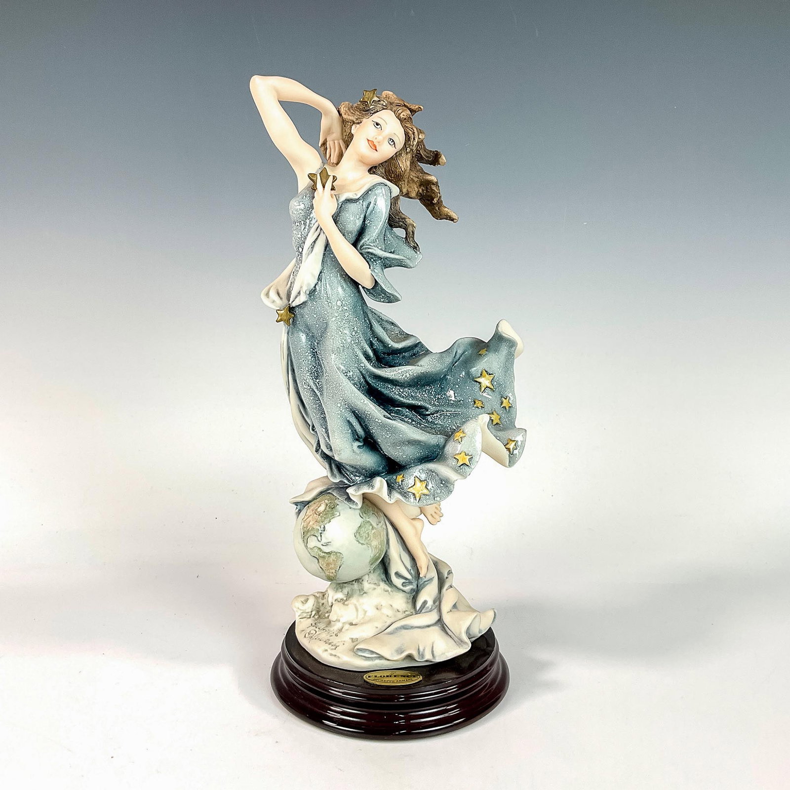 Capodimonte Giuseppe Armani Figurine, Celeste: Matte and glossy finished figurine. Modeled as a beautiful dark haired woman floating above a tiny Earth wearing a blue dress with yellow star decorations. Fixed to round dark wood base. Giuseppe Arma