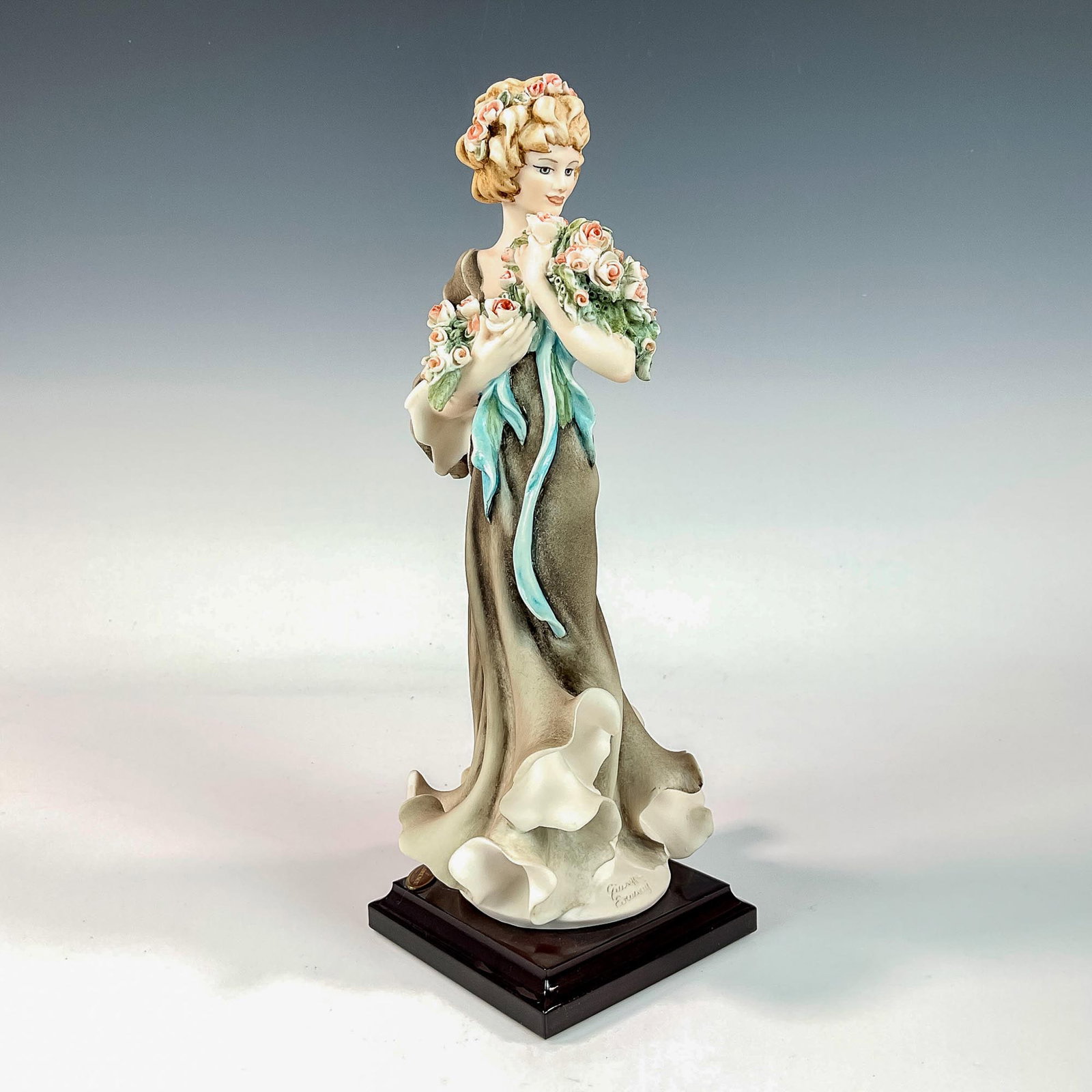 Capodimonte Giuseppe Armani Figurine, Girl with Roses: Matte finished figurine modeled as woman with coy expression wearing a brown frilled dress holding a bouquet of pink roses. Fixed to square dark wood base. Giuseppe Armani impressed to base and Capodi