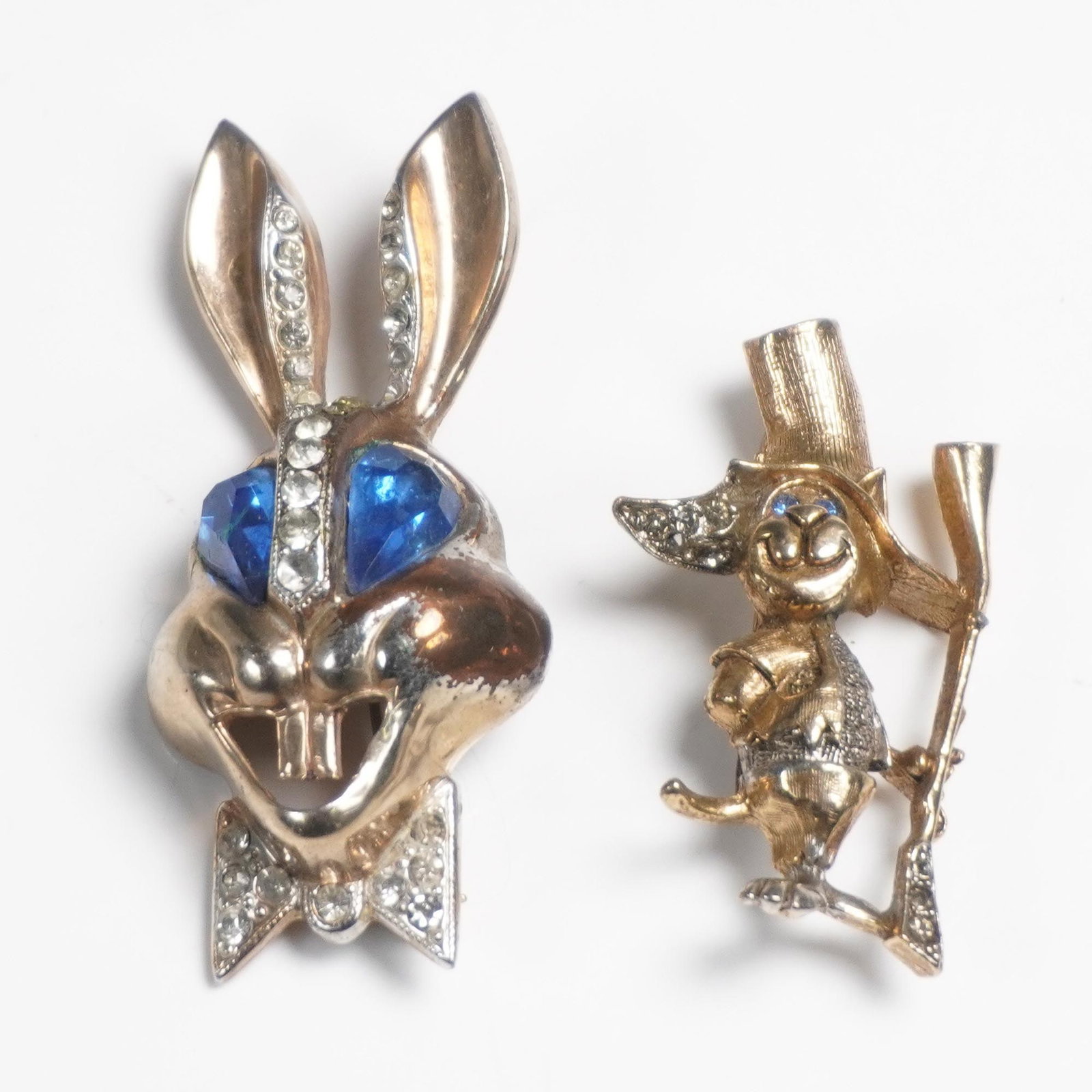 2pc Karu and Figural Character Pins: Two vintage figural character pins. The first is a whimsical rabbit pin with large blue rhinestone eyes, a bow tie, and embedded clear rhinestones along the ears and collar. It is signed Karu Arke Inc