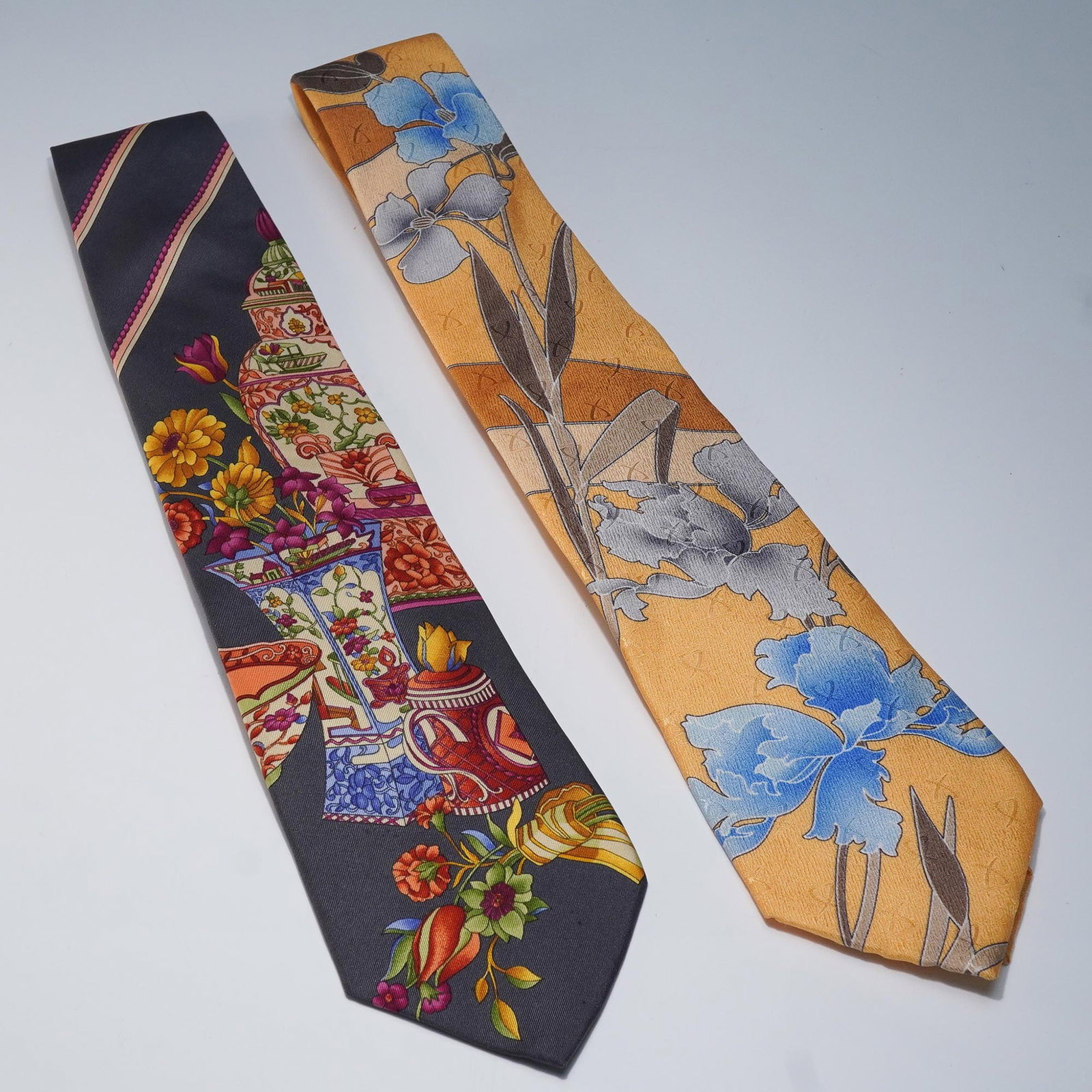 2pc Leonard Paris Silk Ties, Floral and Still Life Patterns: Pair of designer ties by Leonard Paris, each crafted in silk and marked with unique Dessin design numbers. One tie features a warm gold background with blue and gray iris-style flowers, labeled Dessin