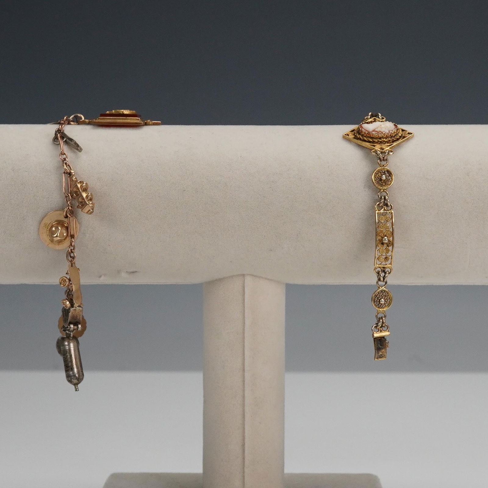 2pc Vintage Gold Tone Cameo and Charm Bracelets: This 2 piece vintage bracelet lot features a gold tone cameo link bracelet and a charm bracelet. The cameo bracelet showcases ornate filigree panels with a raised carved cameo centerpiece, likely resi