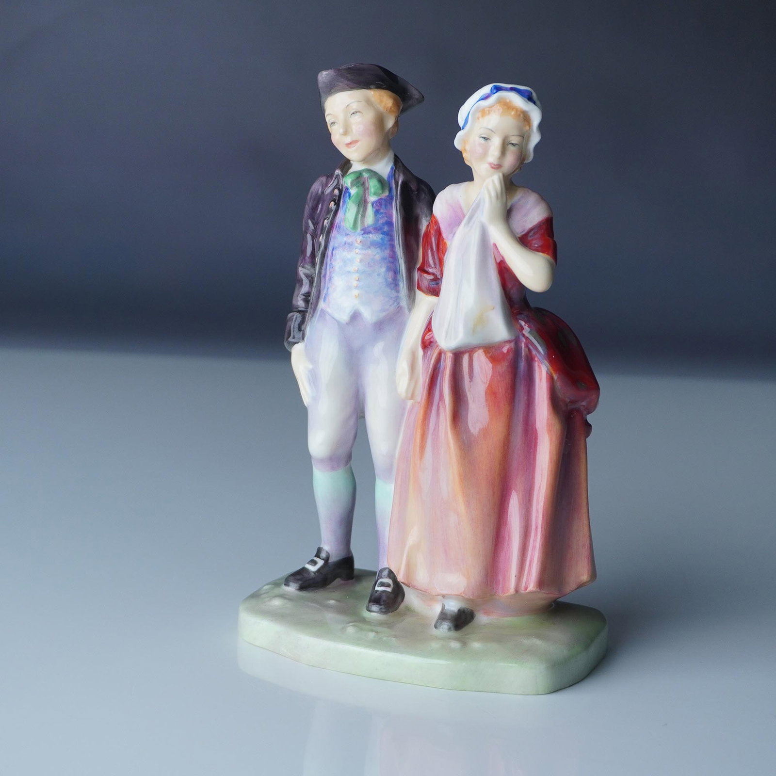 A Courting HN2004 - Royal Doulton Figurine: Royal Doulton A Courting (HN2004), a charming hand-painted figurine designed by Leslie Harradine. This piece depicts a young courting couple in 18th-century attire, capturing a moment of romance with 