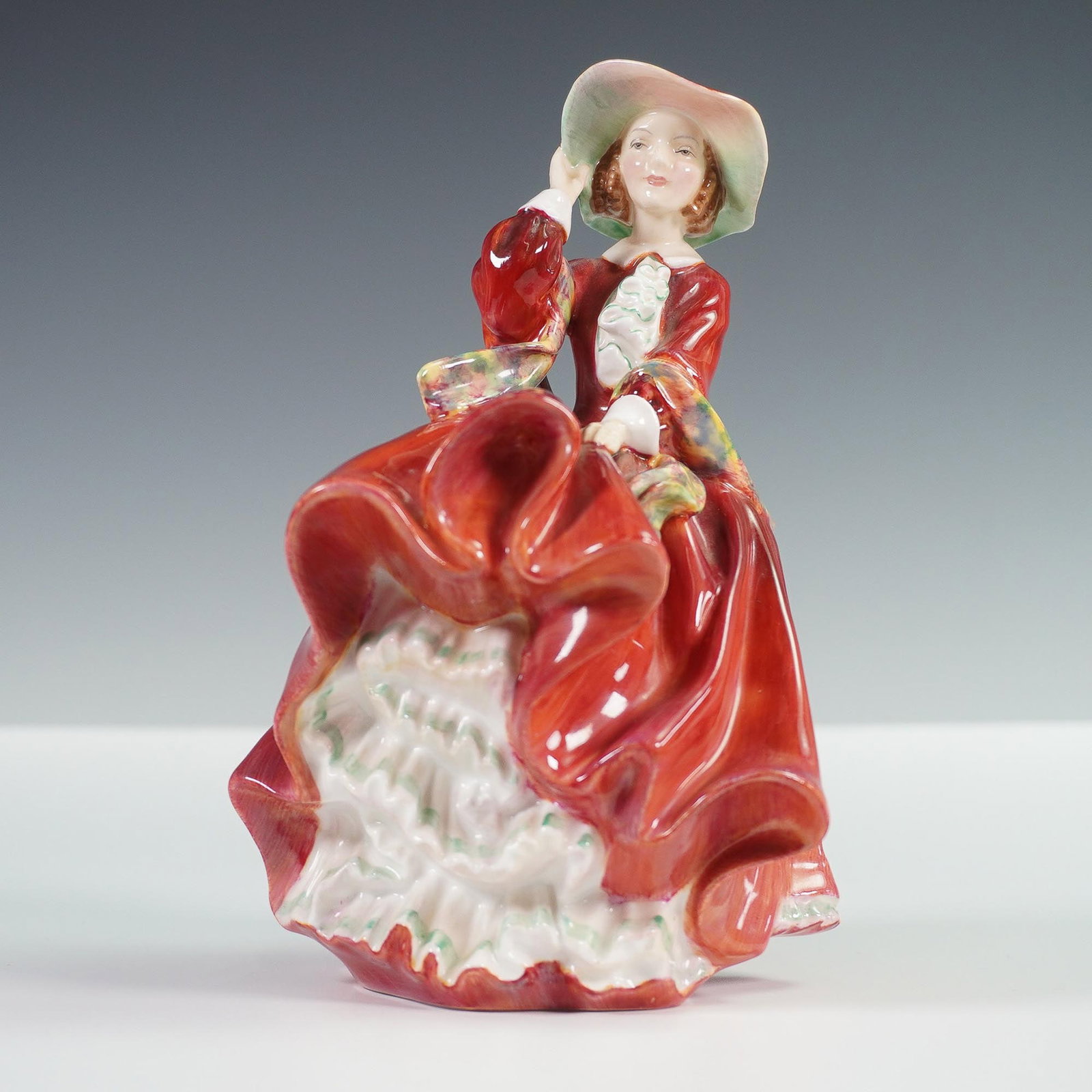 Top o' the Hill HN1834 - Royal Doulton Figurine: Royal Doulton bone china figurine titled Top o' the Hill, model HN1834, designed by Leslie Harradine. First issued in 1937, this classic piece captures a young woman in a flowing red dress and wide-br