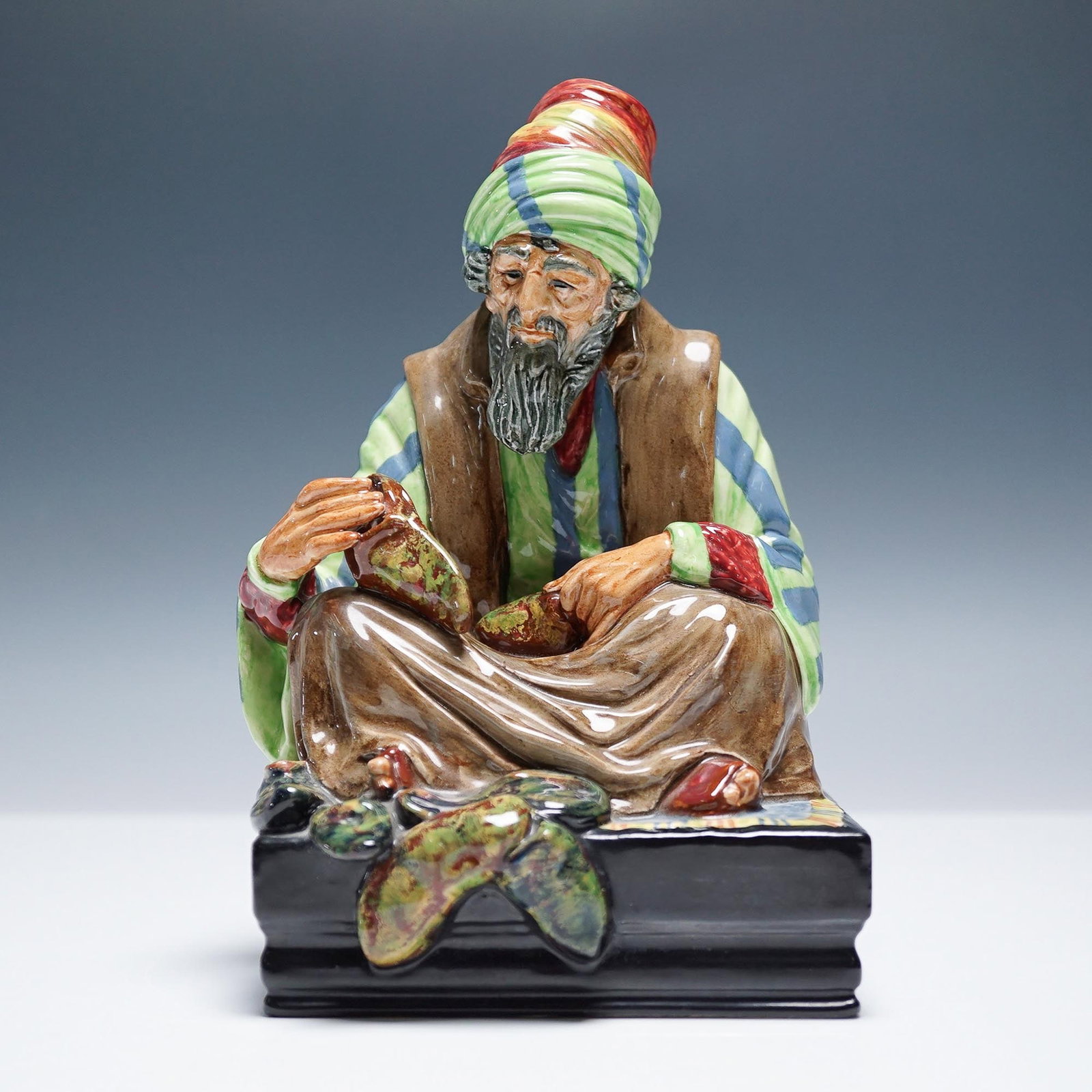 Cobbler HN1706 - Royal Doulton Figurine: This striking Royal Doulton figurine, titled Cobbler (HN1706), depicts a seated elderly man skillfully repairing a shoe, with tools and finished pairs scattered at his feet. Richly hand-painted in vib