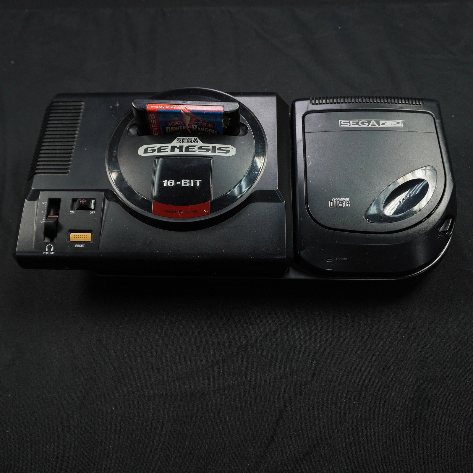 2pc Sega Genesis Console, Includes CD Add-On and Power Rangers Game: Sega Genesis Model 1 console paired with the Sega CD add-on unit, along with a cartridge of Mighty Morphin Power Rangers. The Genesis system is a 16-bit platform known for its iconic library of action