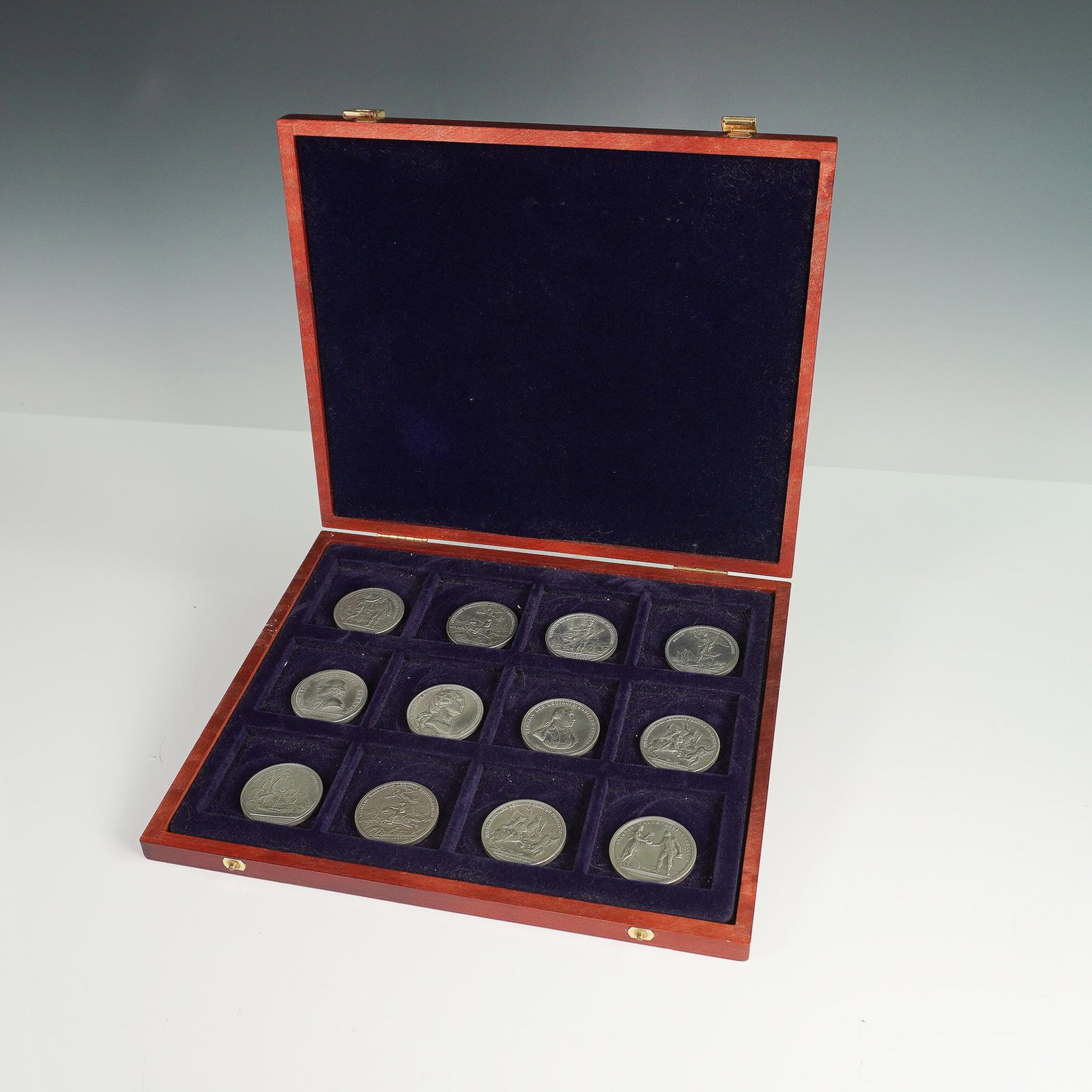 12pc Replica Comitia Americana Pewter Medals in Case: Twelve-piece collection of replica Comitia Americana pewter medals presented in a fitted wooden case with blue velvet-lined compartments. The set includes one Henry Lee at Paulus Hook medal, one Horat