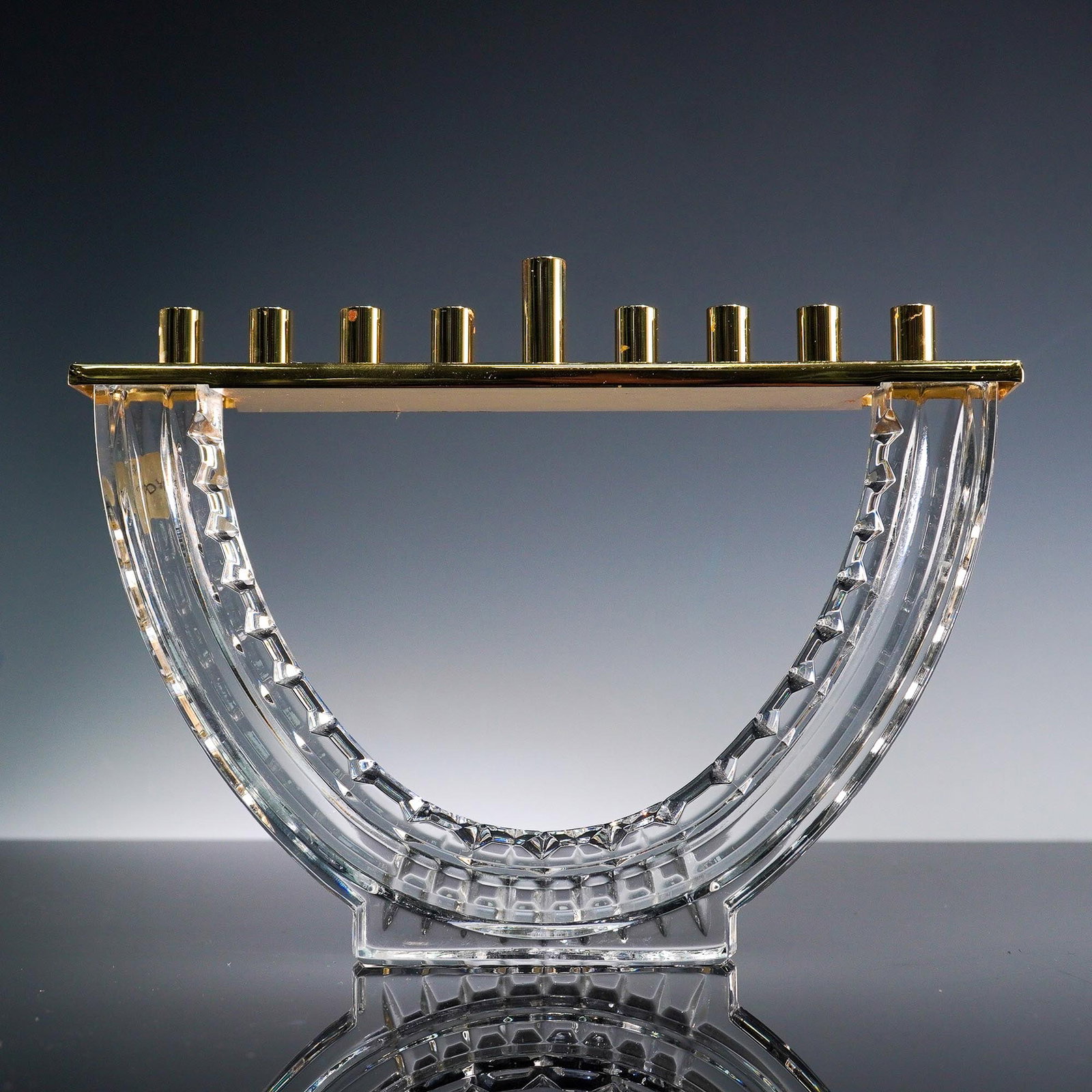 Waterford Crystal and Brass Judaica Menorah: Elegant Judaica menorah by Waterford, featuring a semi-circular clear crystal base with precision-cut facets and geometric detailing, supporting a sleek brass candleholder bar with nine cylindrical ho