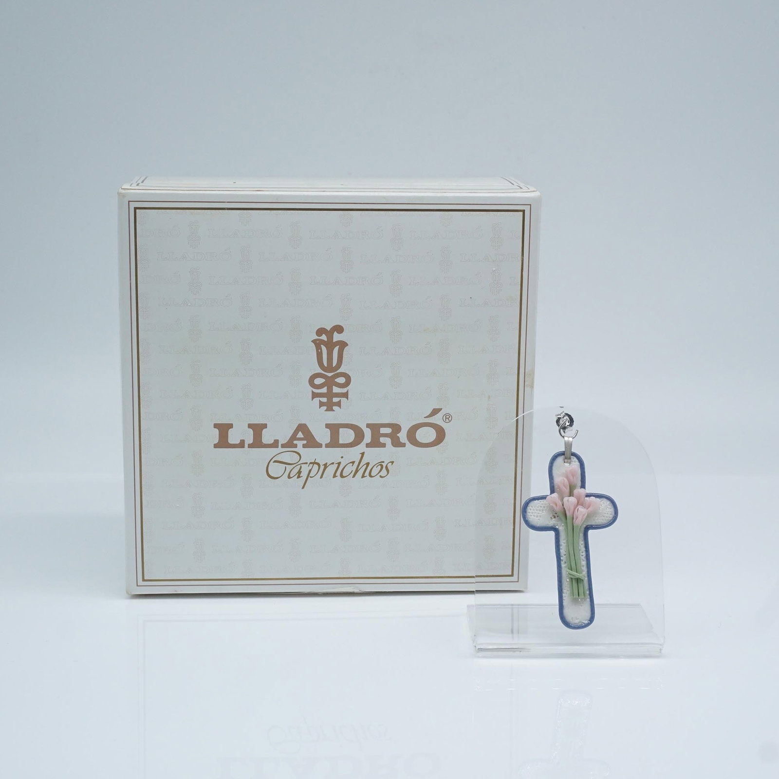 Lladro Porcelain Pendant, Ornate Cross #8 01001656: Lladro porcelain pendant #01001656, Ornate Cross #8, featuring a delicately sculpted cross adorned with soft pastel flowers and a fine blue border. This elegant piece captures the timeless beauty of L